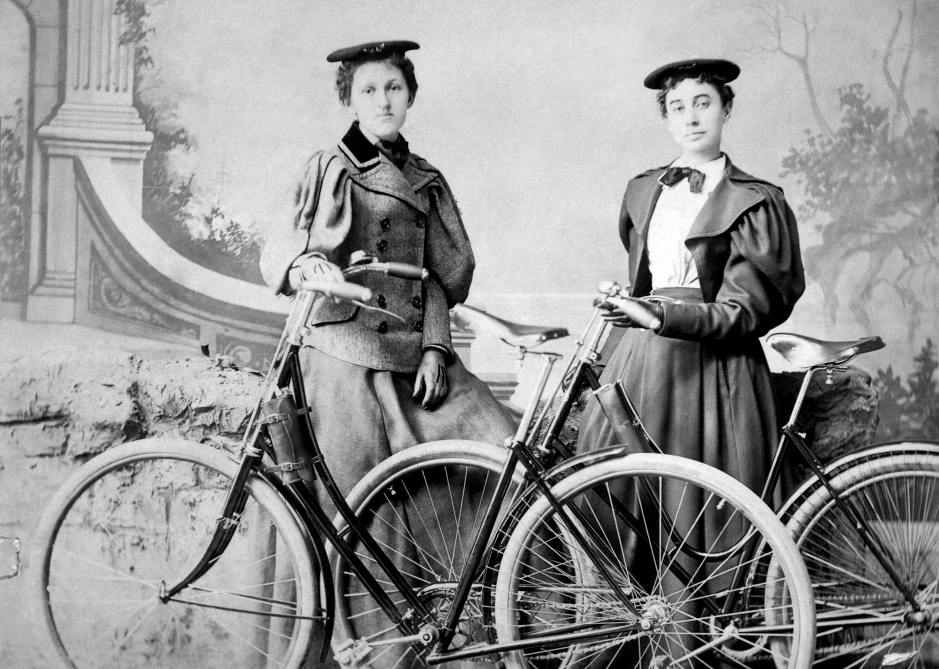 two women in old clothing standing by their bicycles