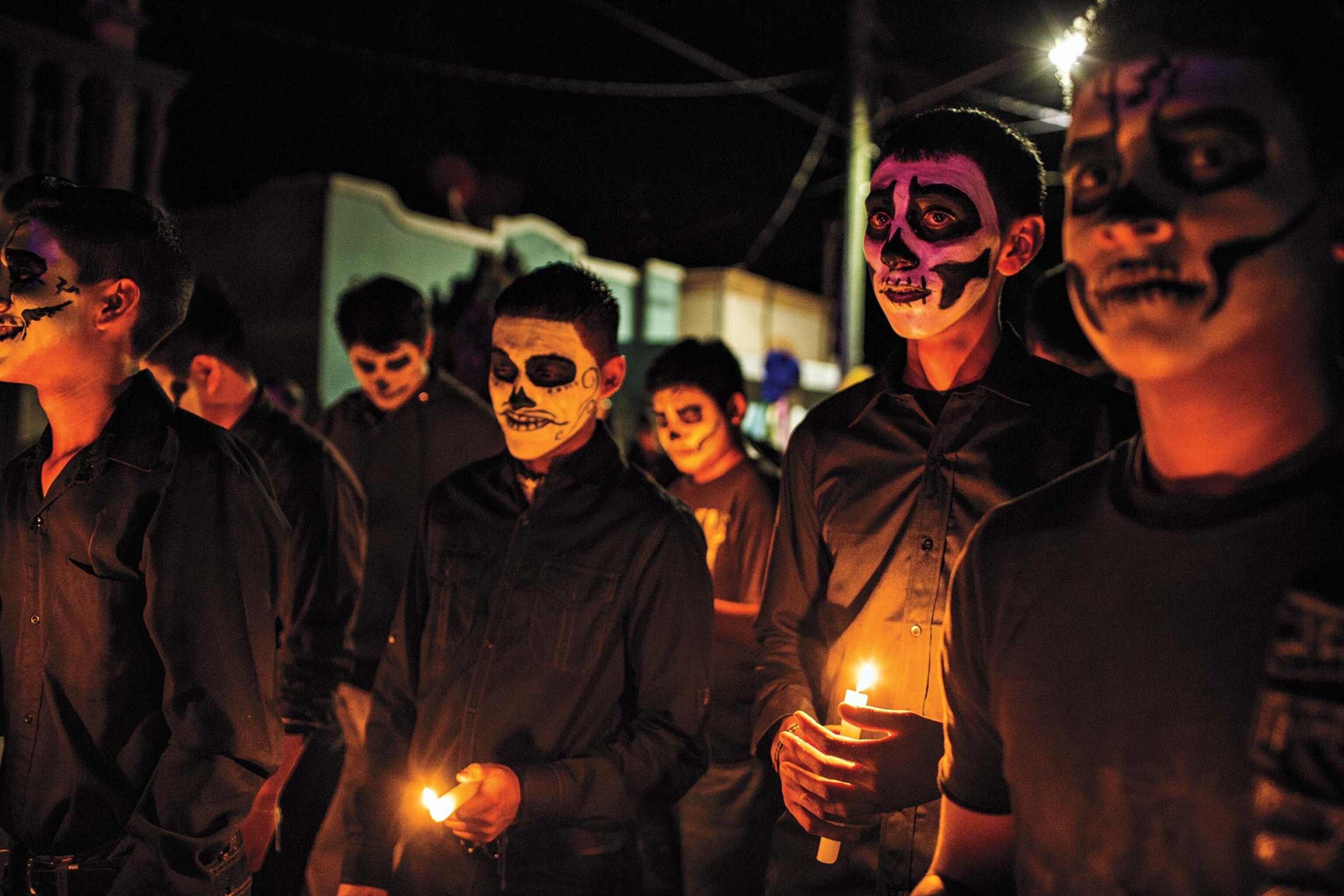 A community in Mexico, with their faces painted as skulls, celebrates Day of the Dead with candles