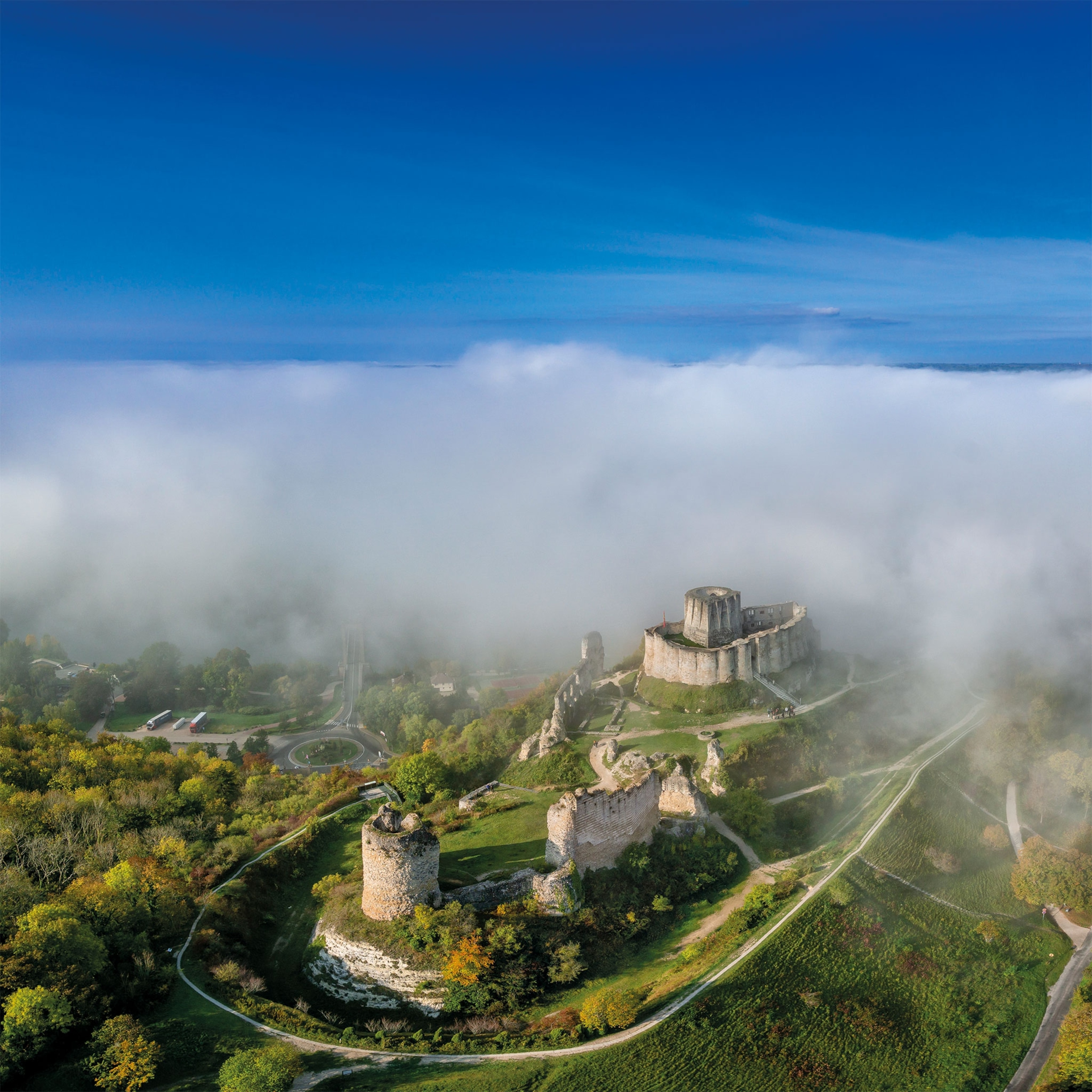 A sky view of a medieval castle on a hill, cloaked in a cloud