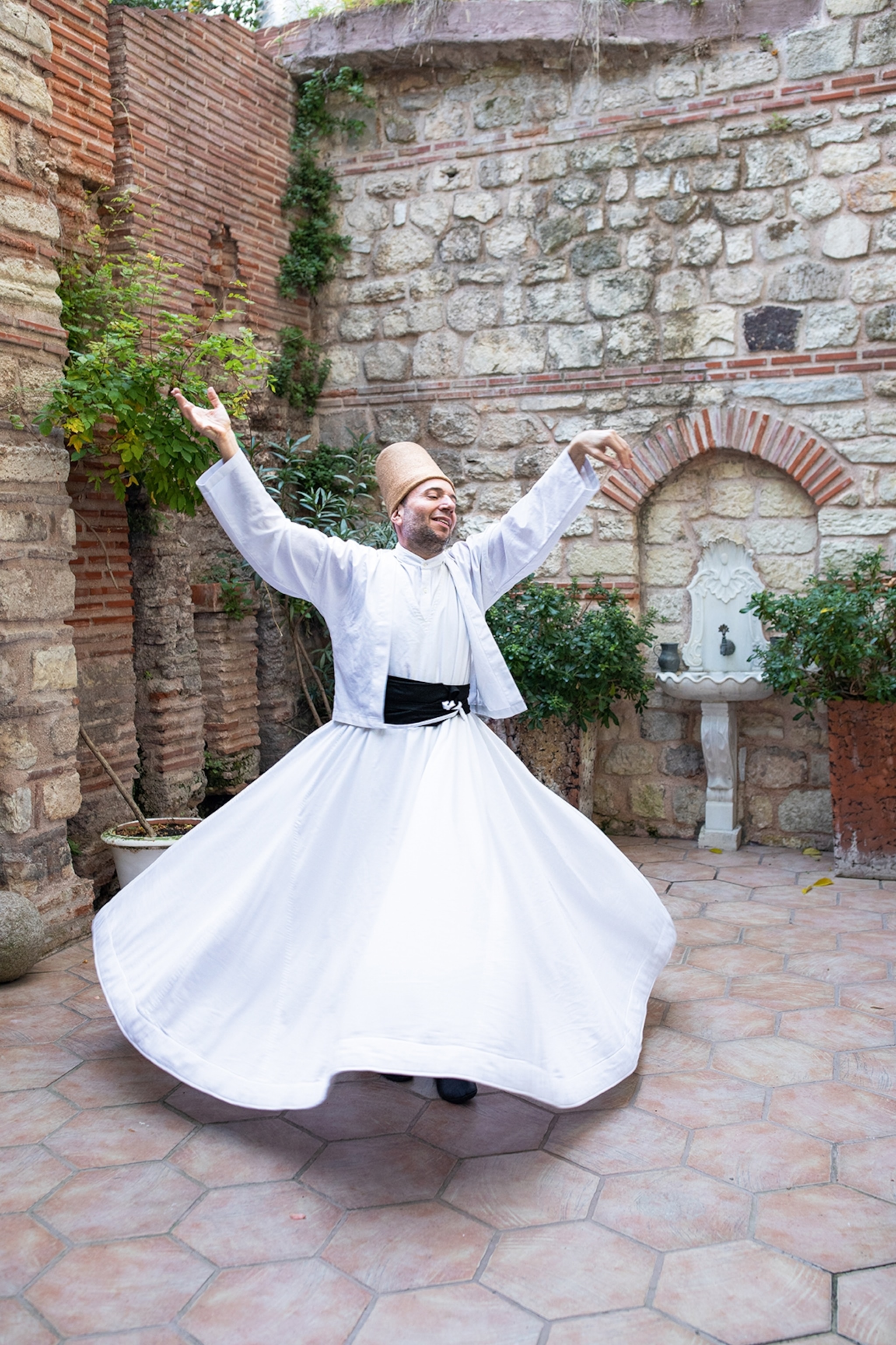 Man wearing a long white dress and jacket in a stone courtyard dancing