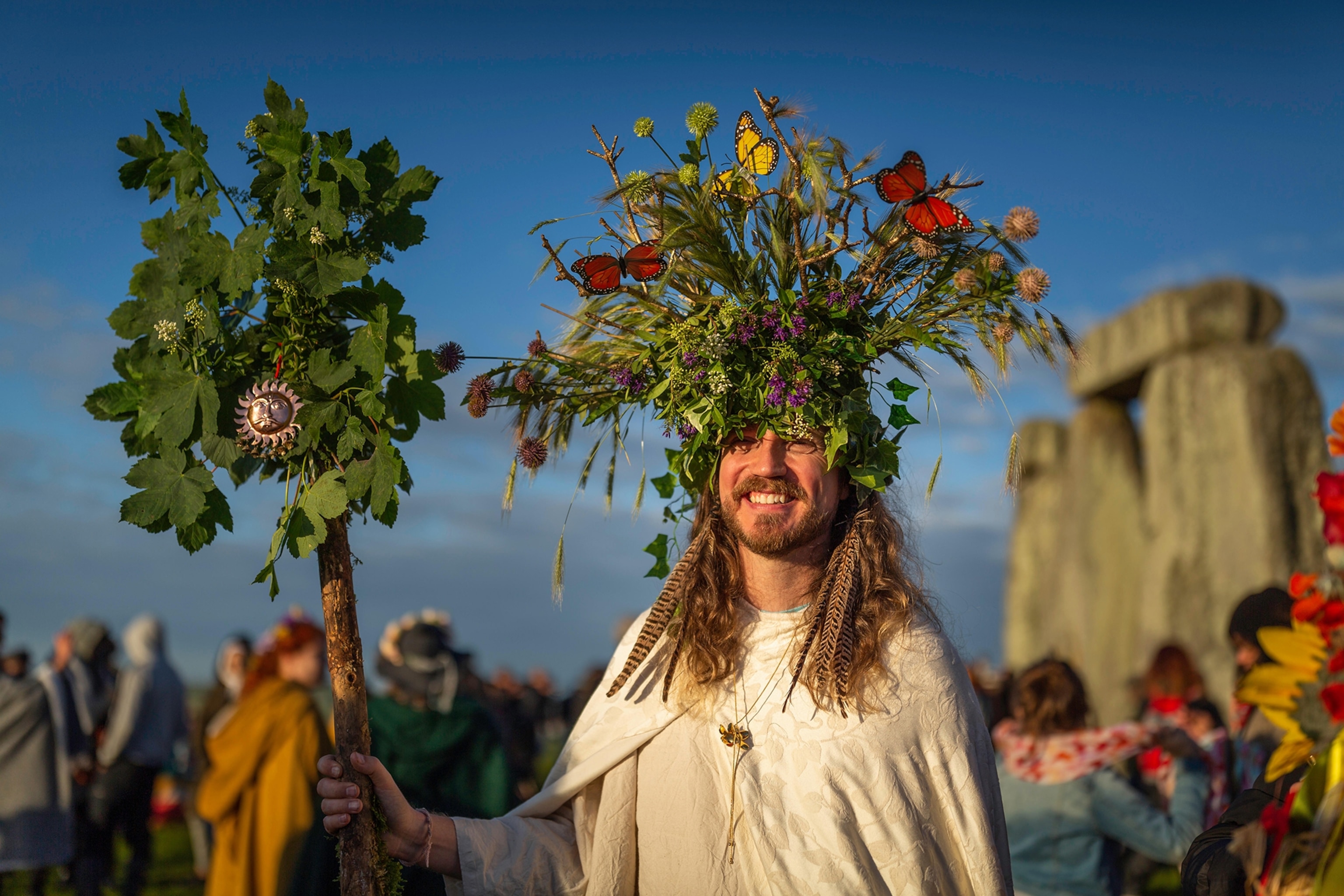 A picture of a beaded man with long hair who is celebrating midsummer. He is wearing a headdress made of plants and flowers.
