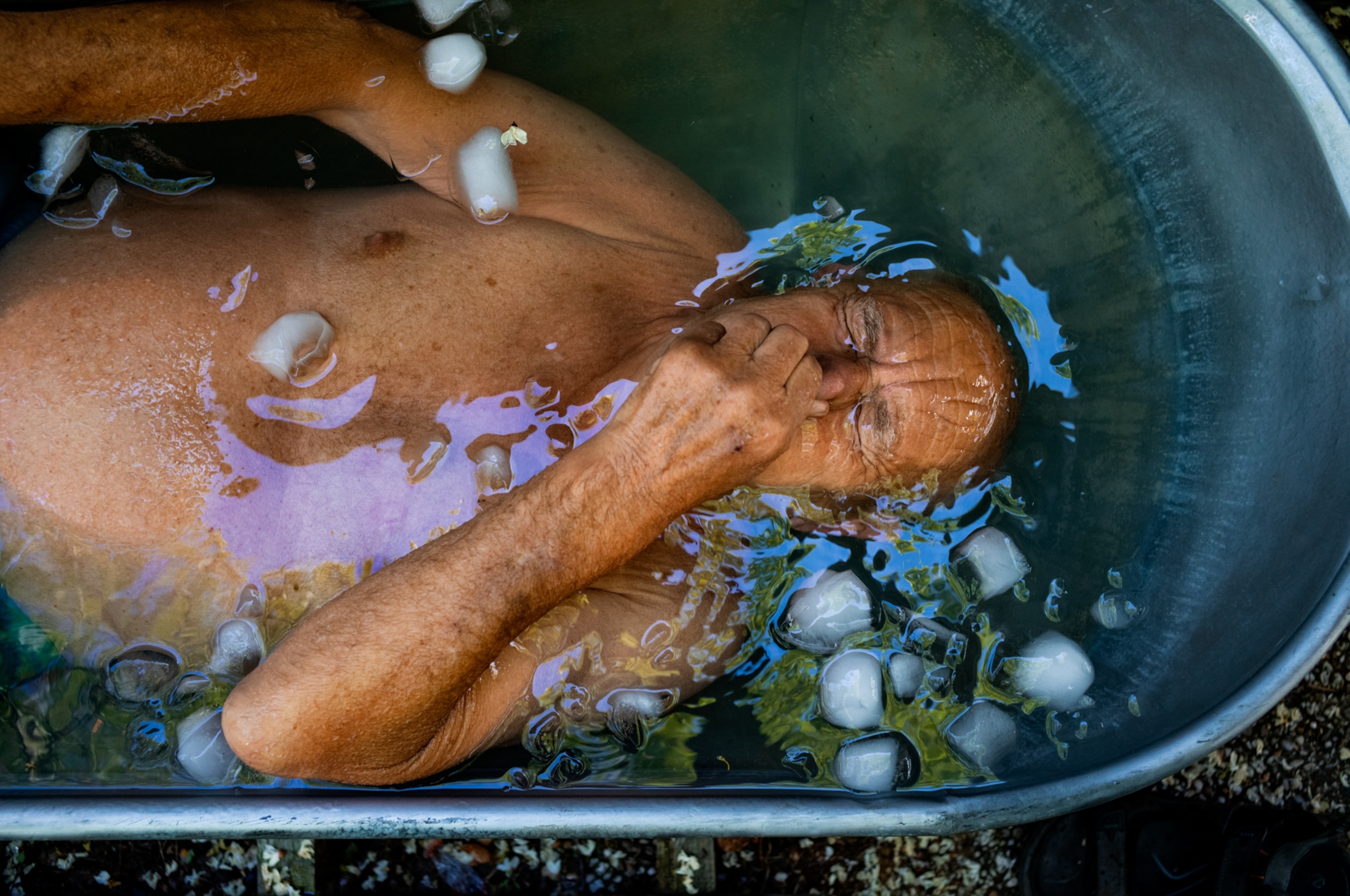 A man is seen from above as he takes an ice bath in an antique, metal tub.