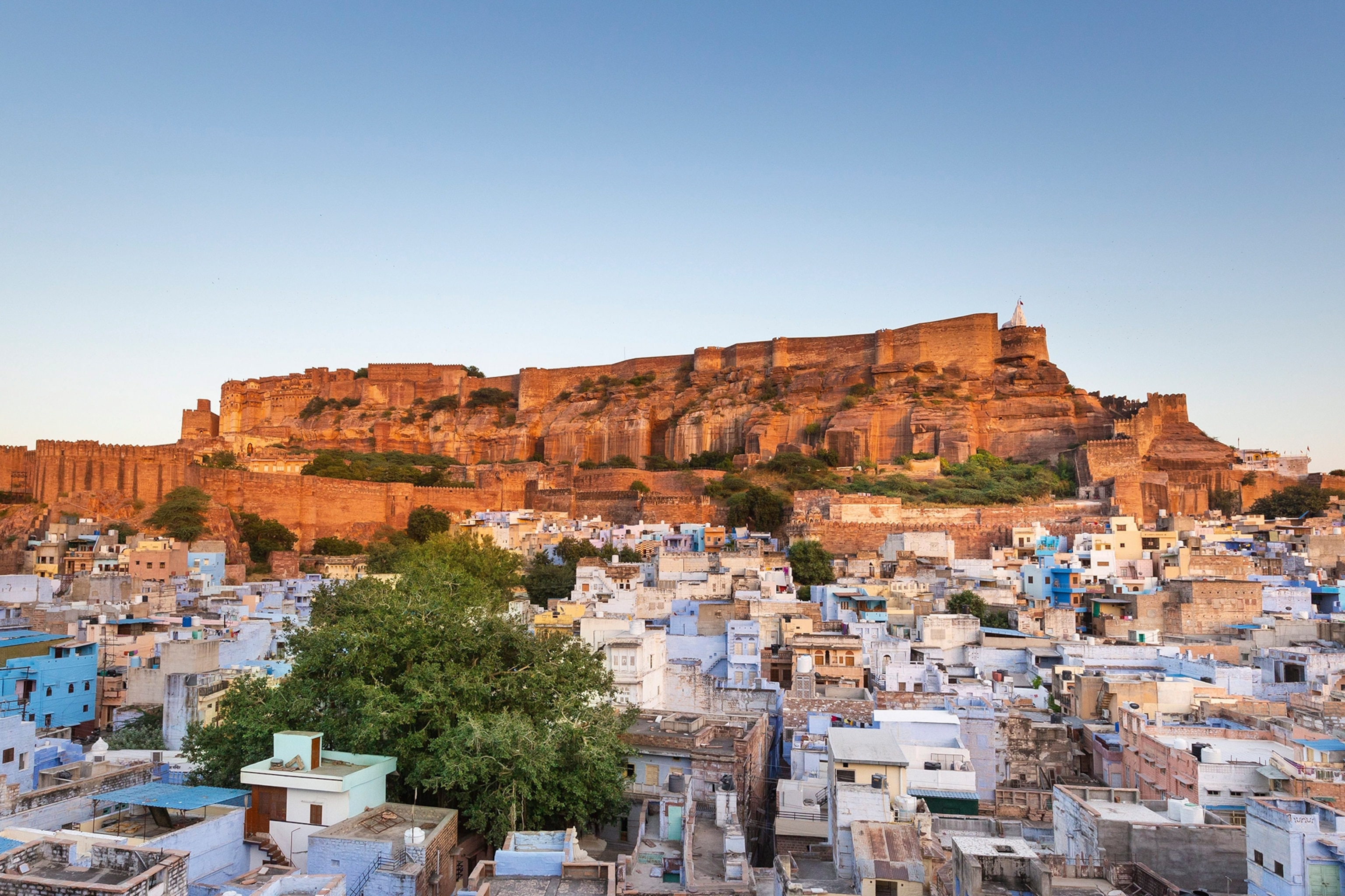A dusk-lit sand palace rising above a flat-roofed cityscape on a wide hill.