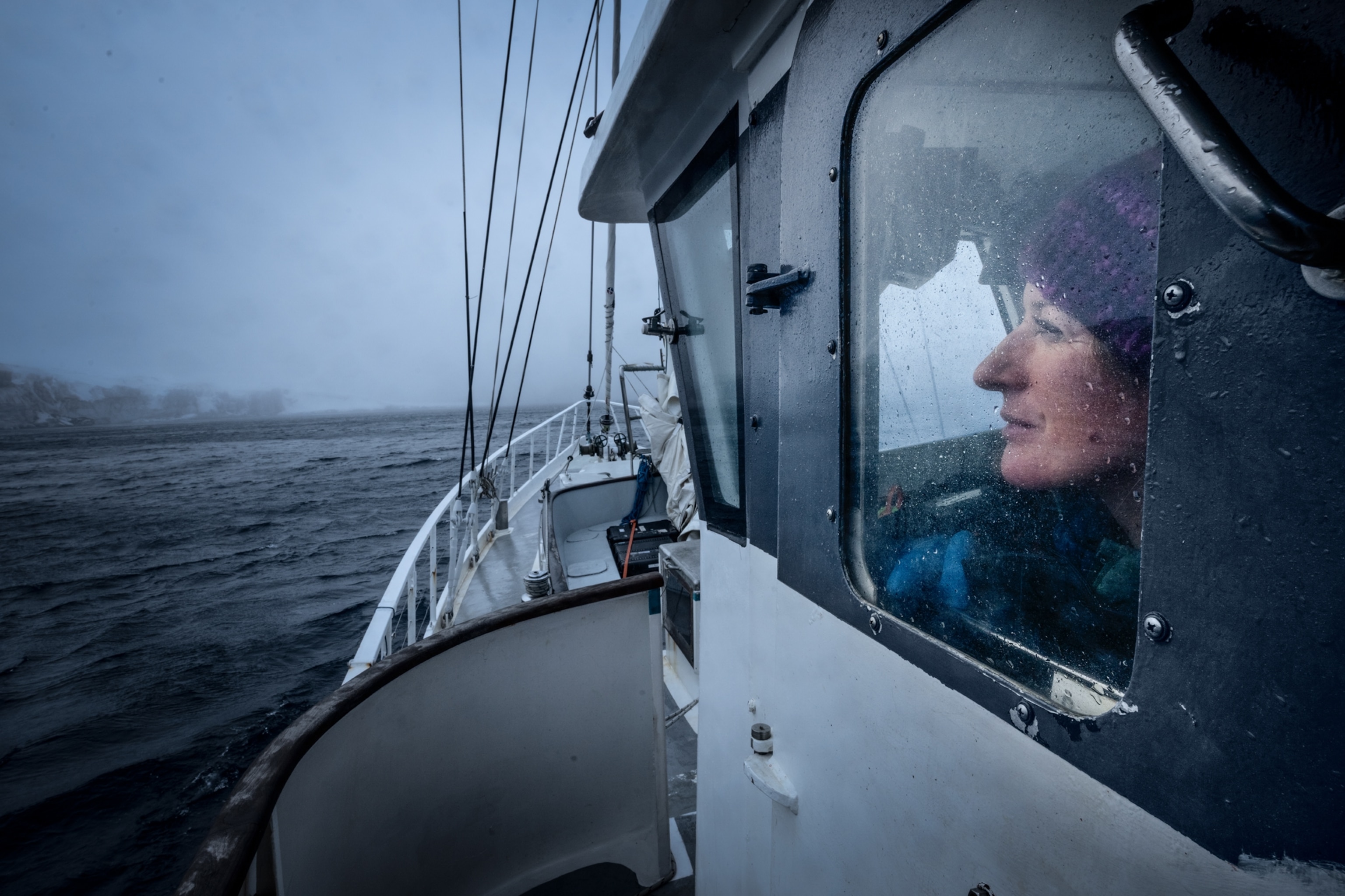 A woman looking through the window at the island while approaching it on the sailboat.