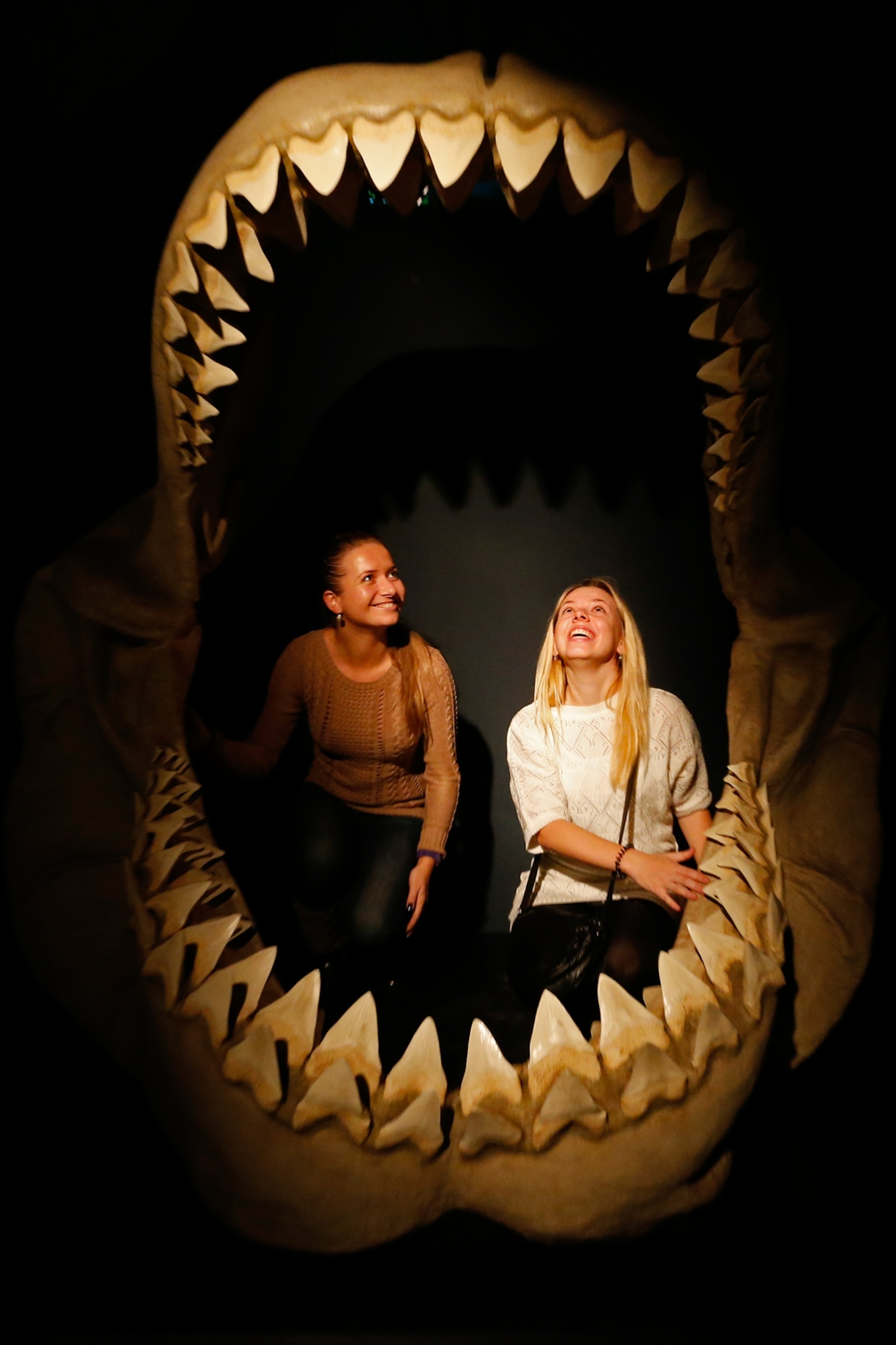Two women standing within a reproduction of the jaws of an enormous shark
