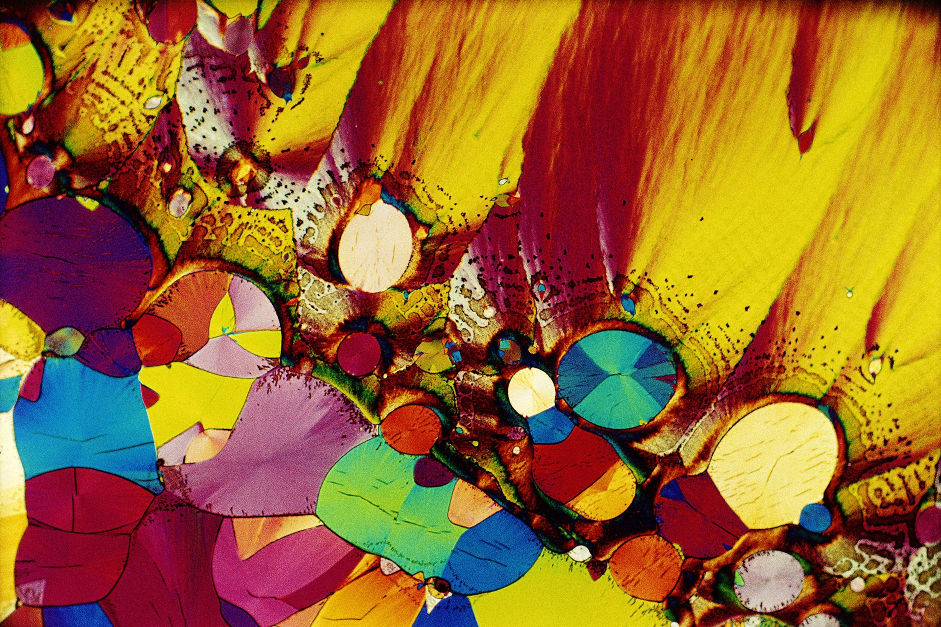 A colorful, kaleidoscope pattern of yellows, blues, pinks, purples and reds run on the bottom half of the image diagonally from left to right and the top half are yellow, orange, and red blocks of color that resemble an aerial view of mountains.