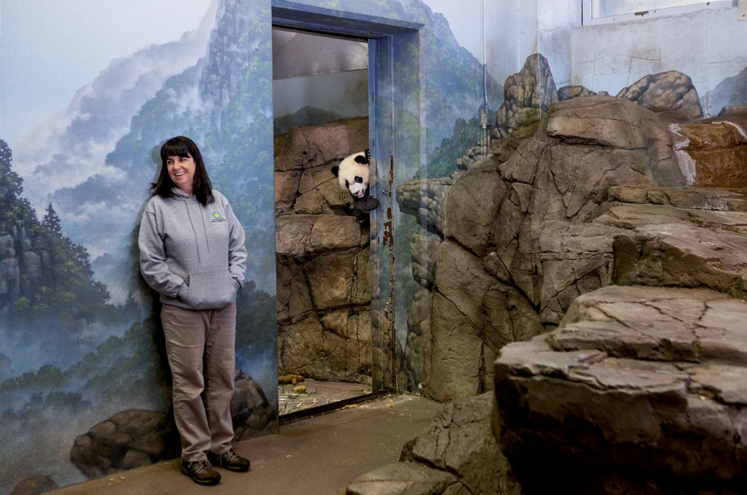 woman leaning against wall mural and panda picking through doorway.