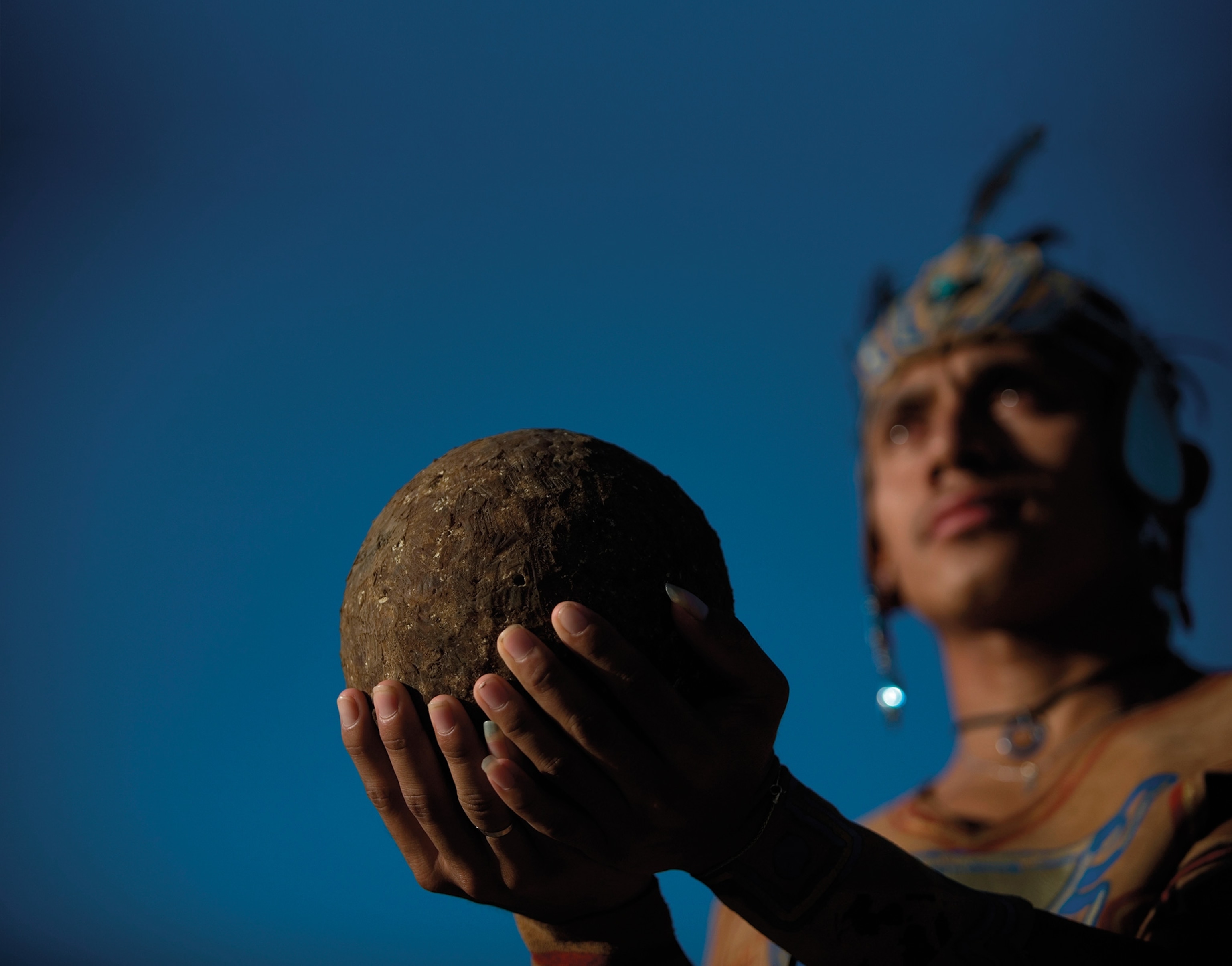 A man wearing Mesoamerican garb holds a ball.
