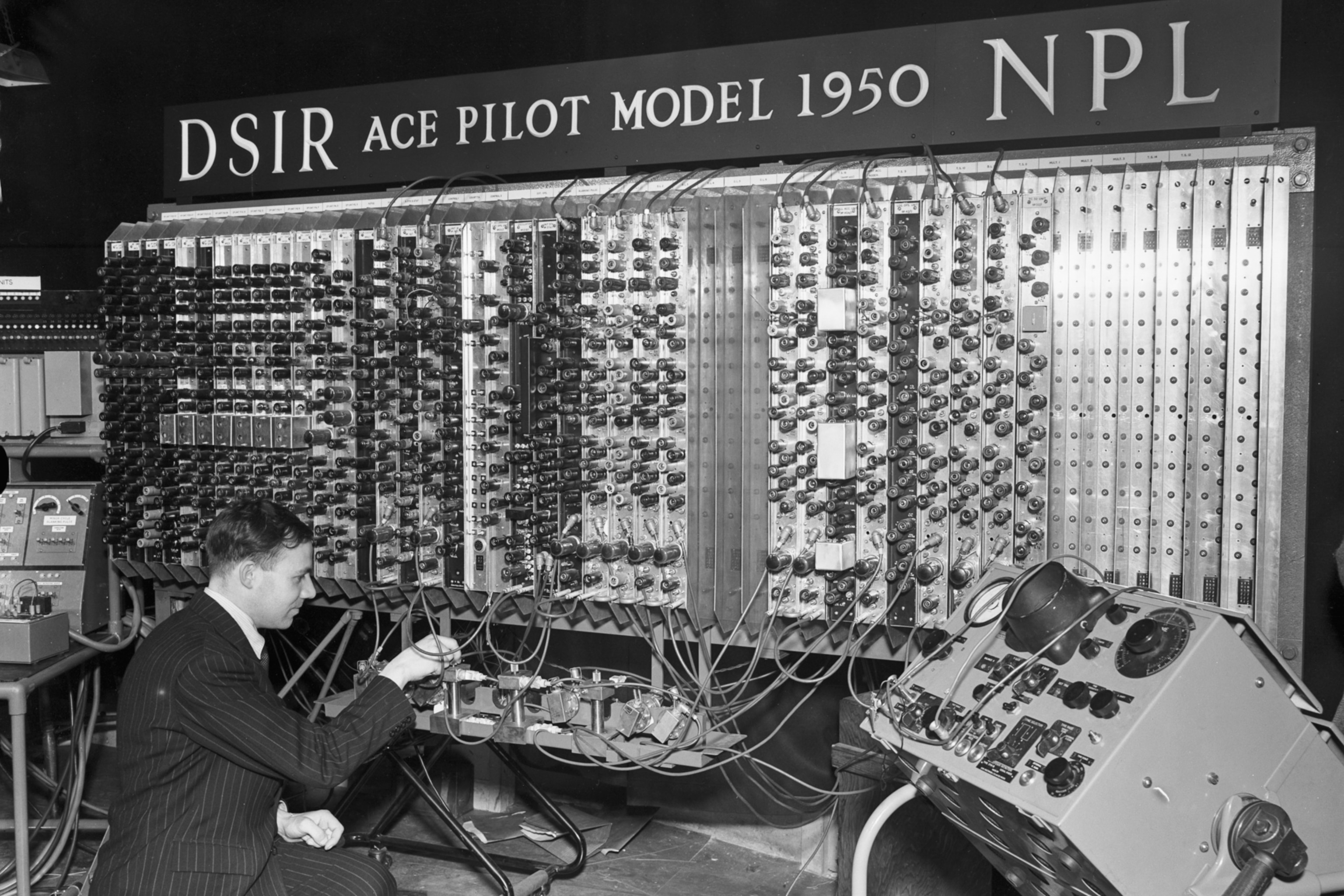 Electronic engineer Edward Newman couches down to inspect part of the Pilot Model ACE computer.