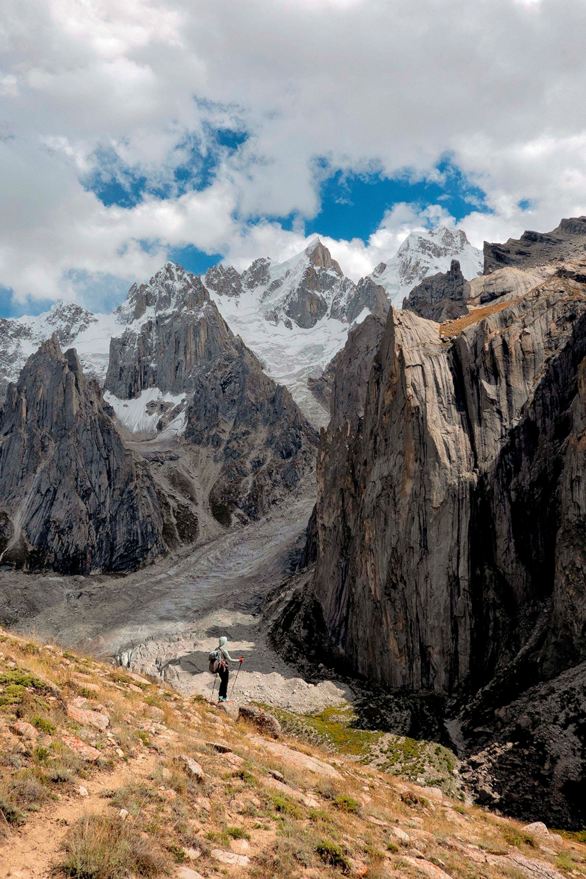 A female hiker standing on a mountain cliff and looking into the stony mountain valley with distant white peaks.