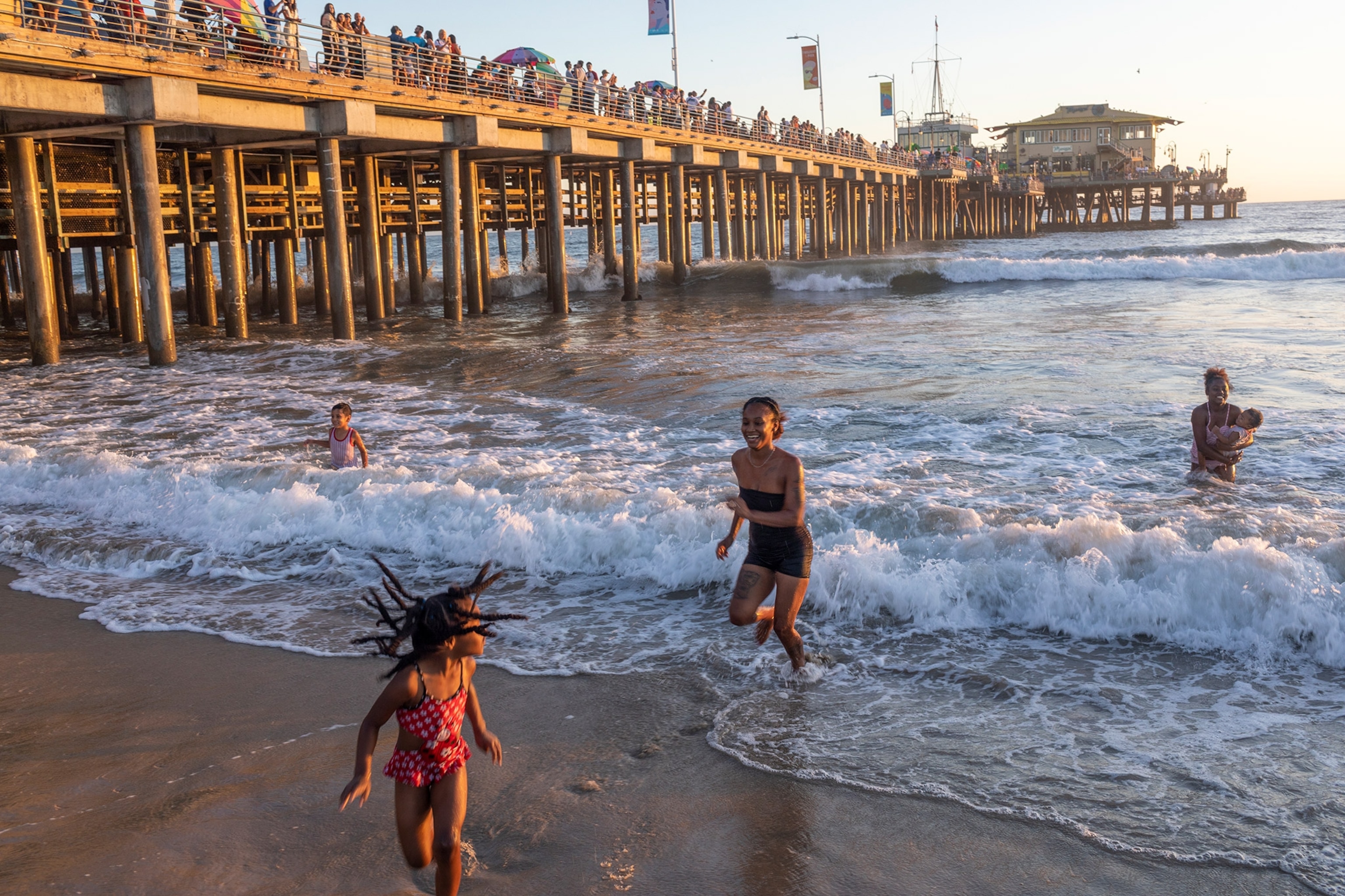 Waves roll in as different members of a family laugh and run on the beach with warm sunlinght.
