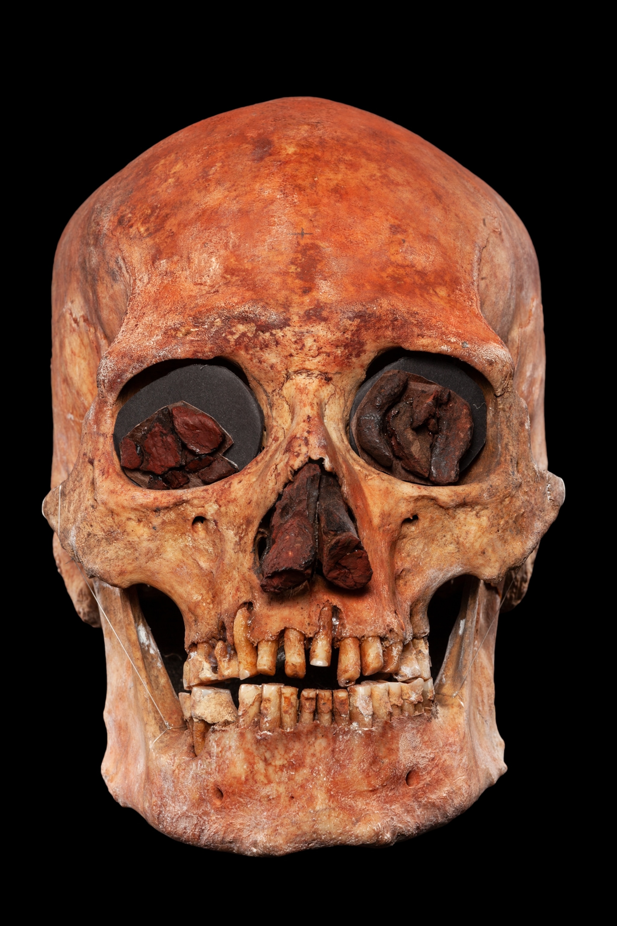 red human skull with eye pits and nasal cavity filled with red clay