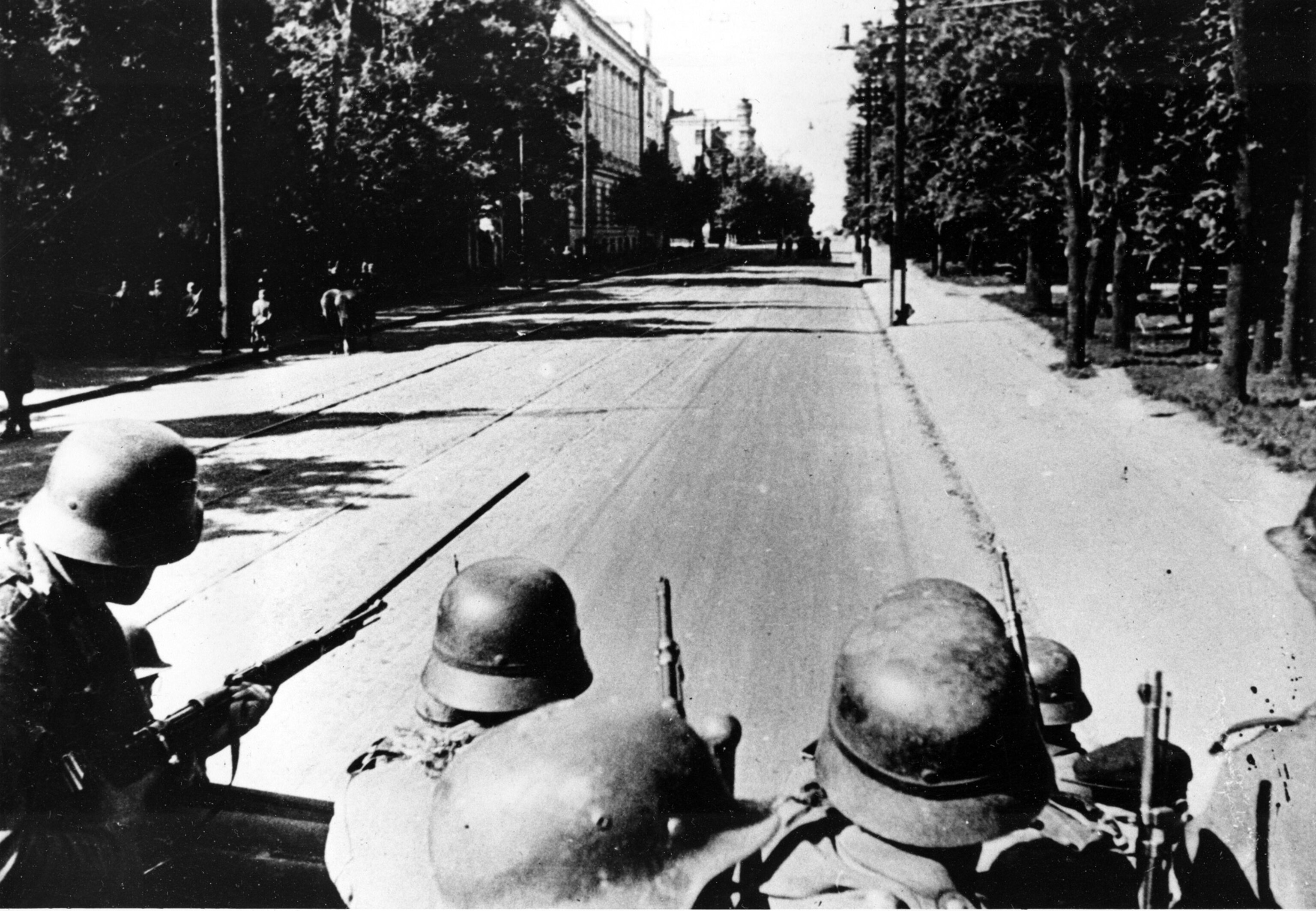 soldiers looking down a street and riding on the back of a truck