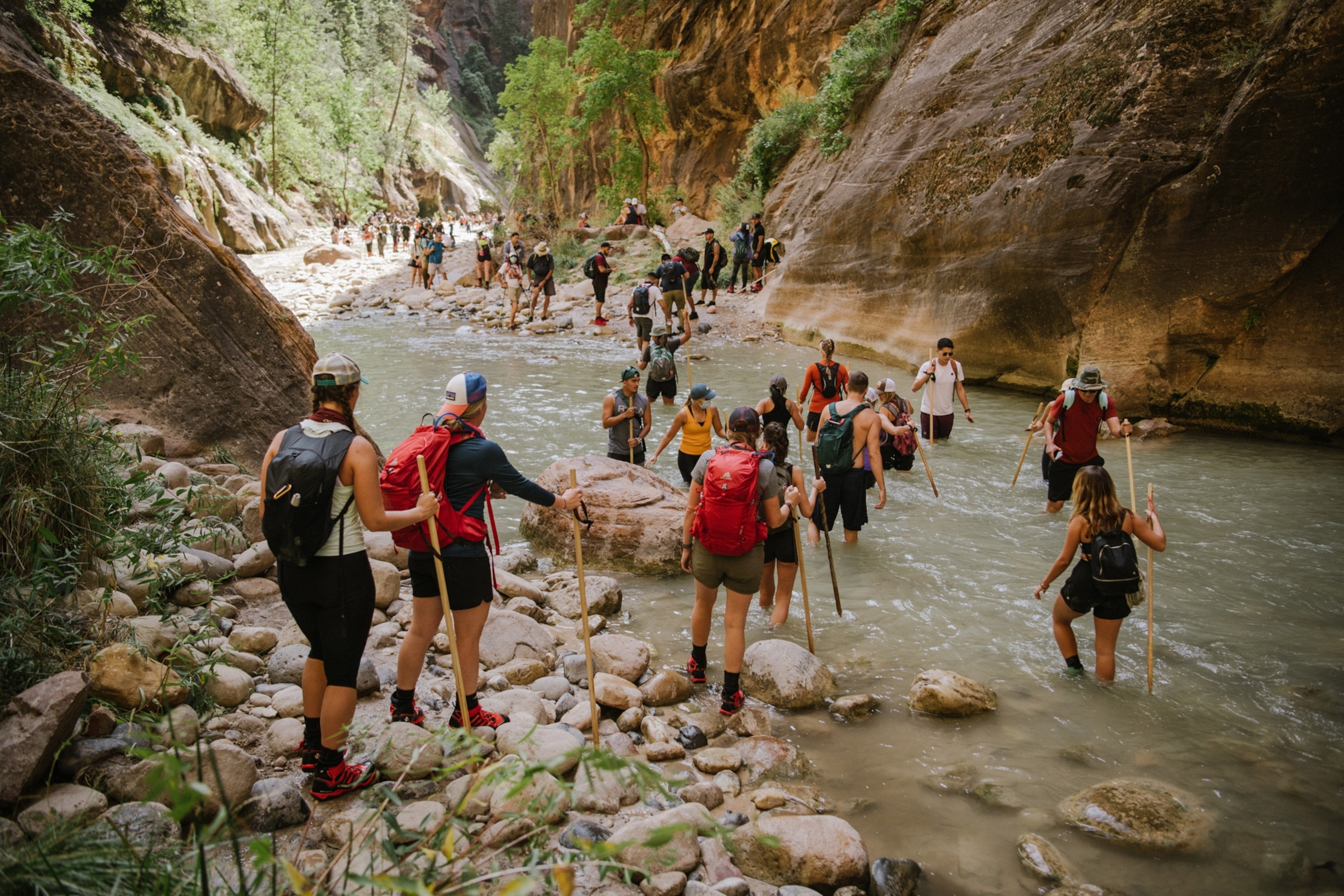 A group of people hiking walking across a river.