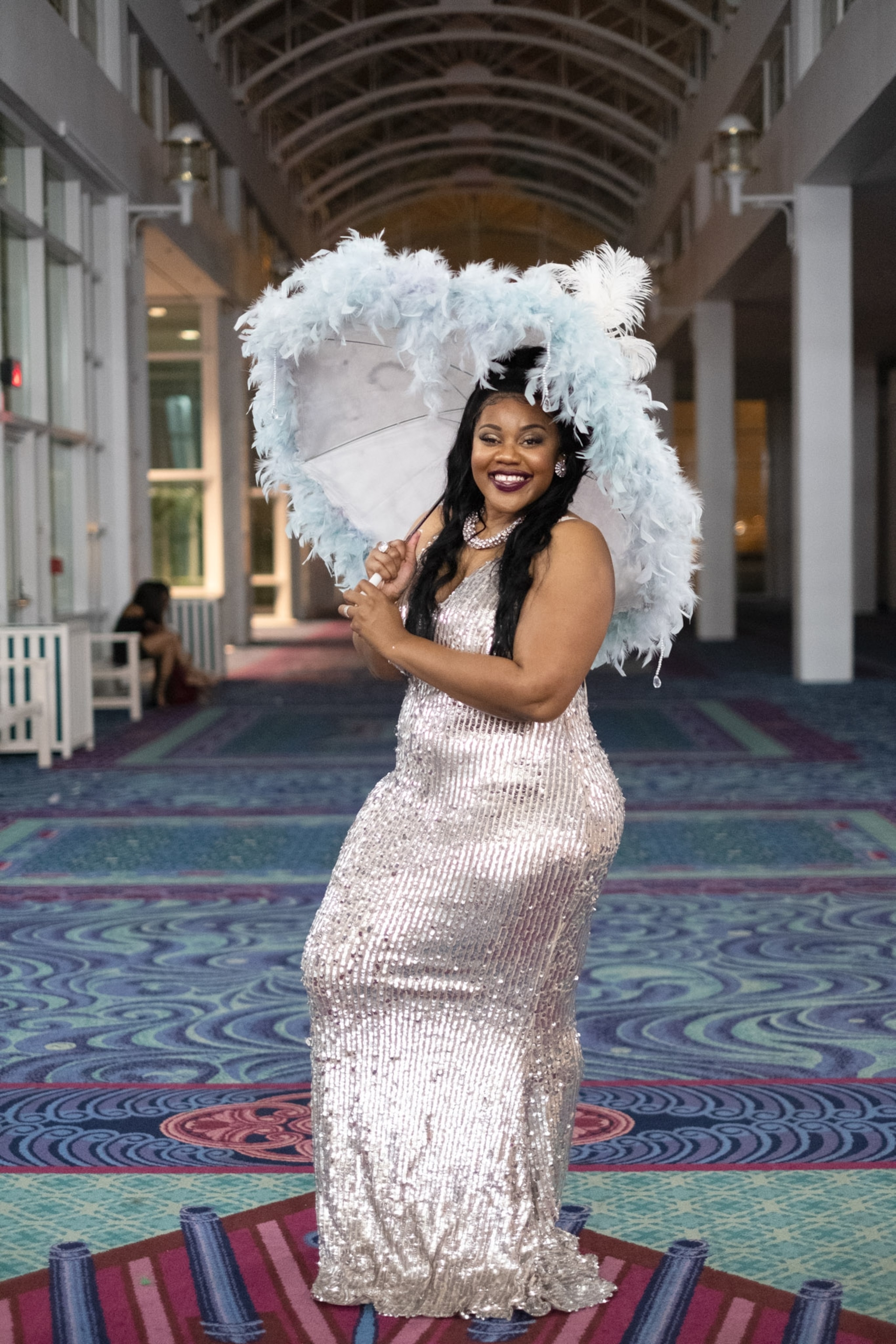 a woman in a long sequenced gown holding up a feathered-edge umbrella