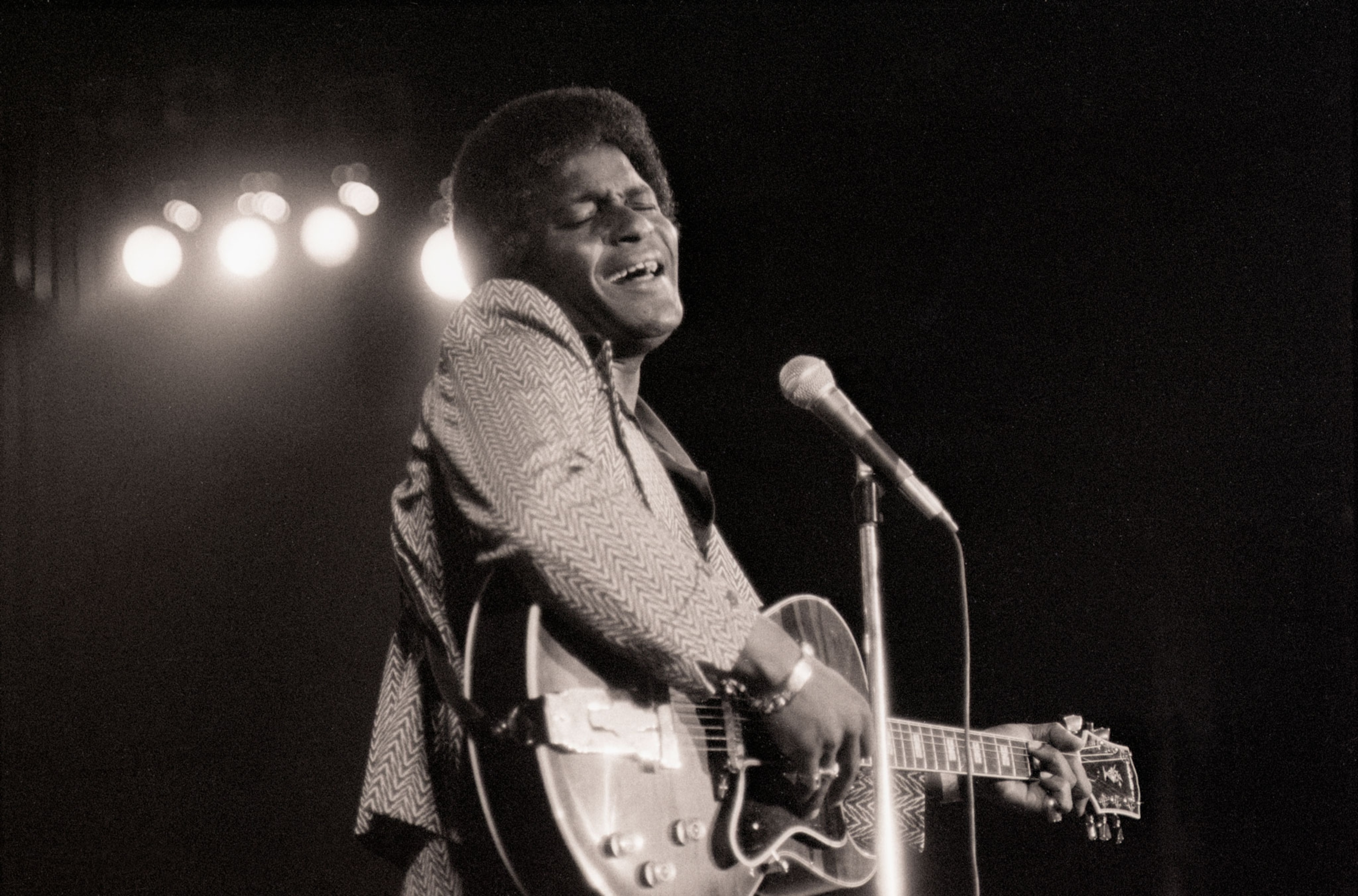 a black and white photograph of a man playing the guitar and signing in front of a microphone
