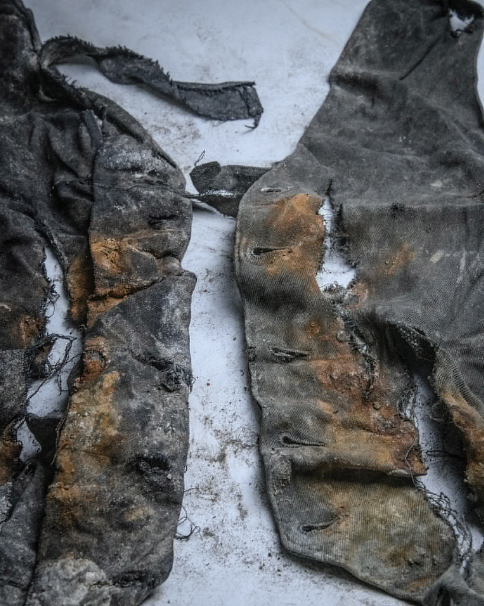 Picture of two cloth jackets blackened from being buried with dark orange stains all along the sides, the jackets are very torn.