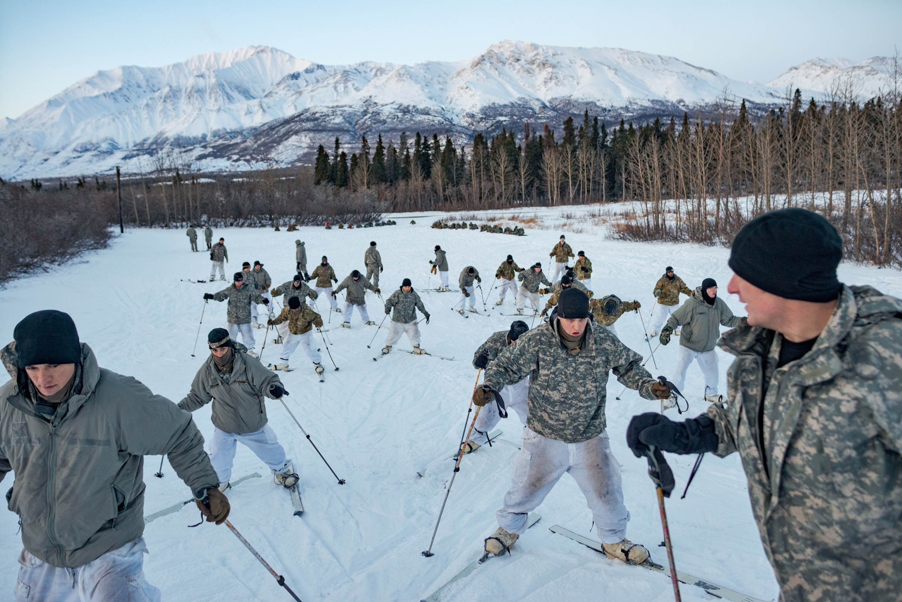 soldiers in winter camouflage jackets on skis going uphill.