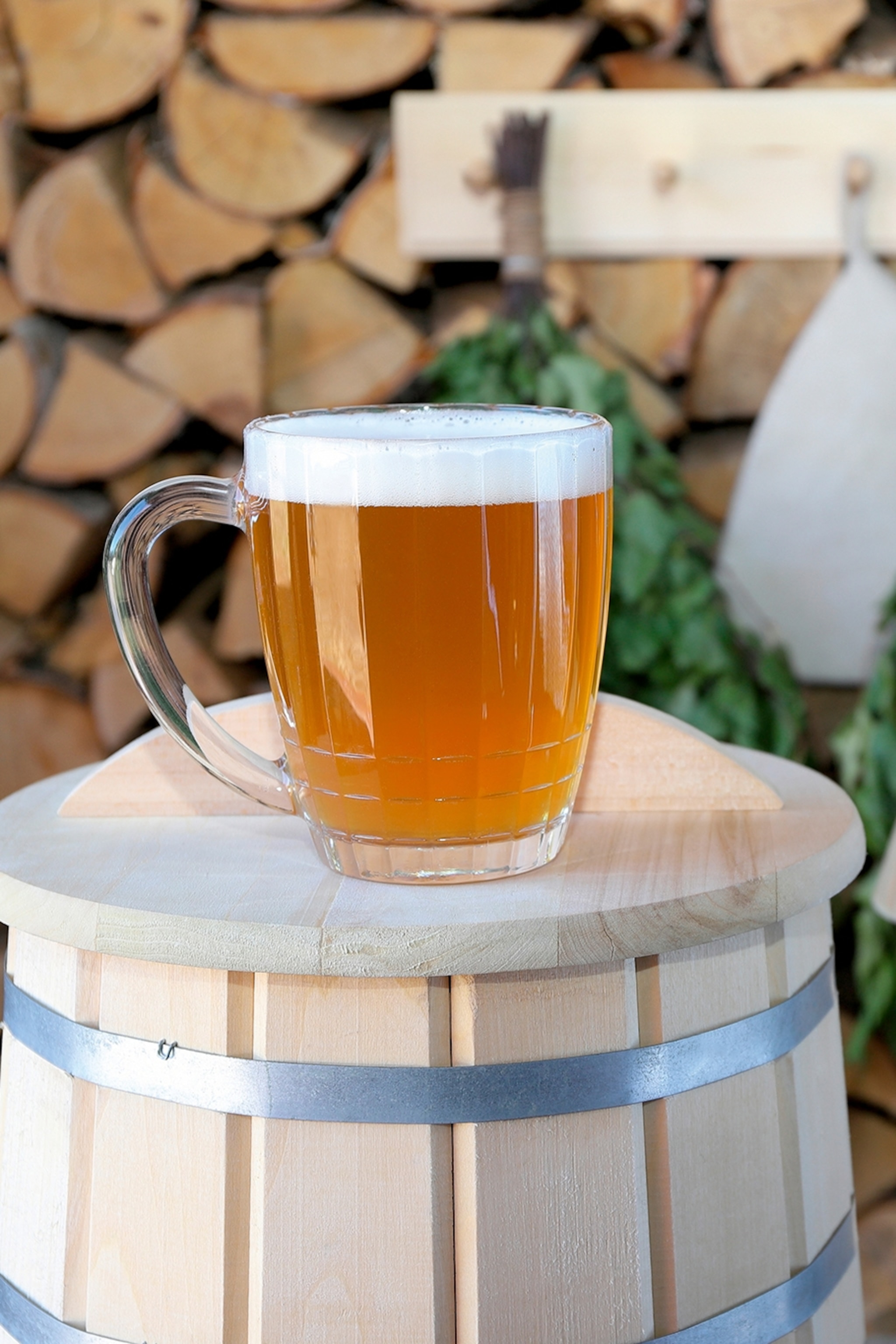 A glass of beer atop a barrel with sauna equipment hung in the back on a log wall.