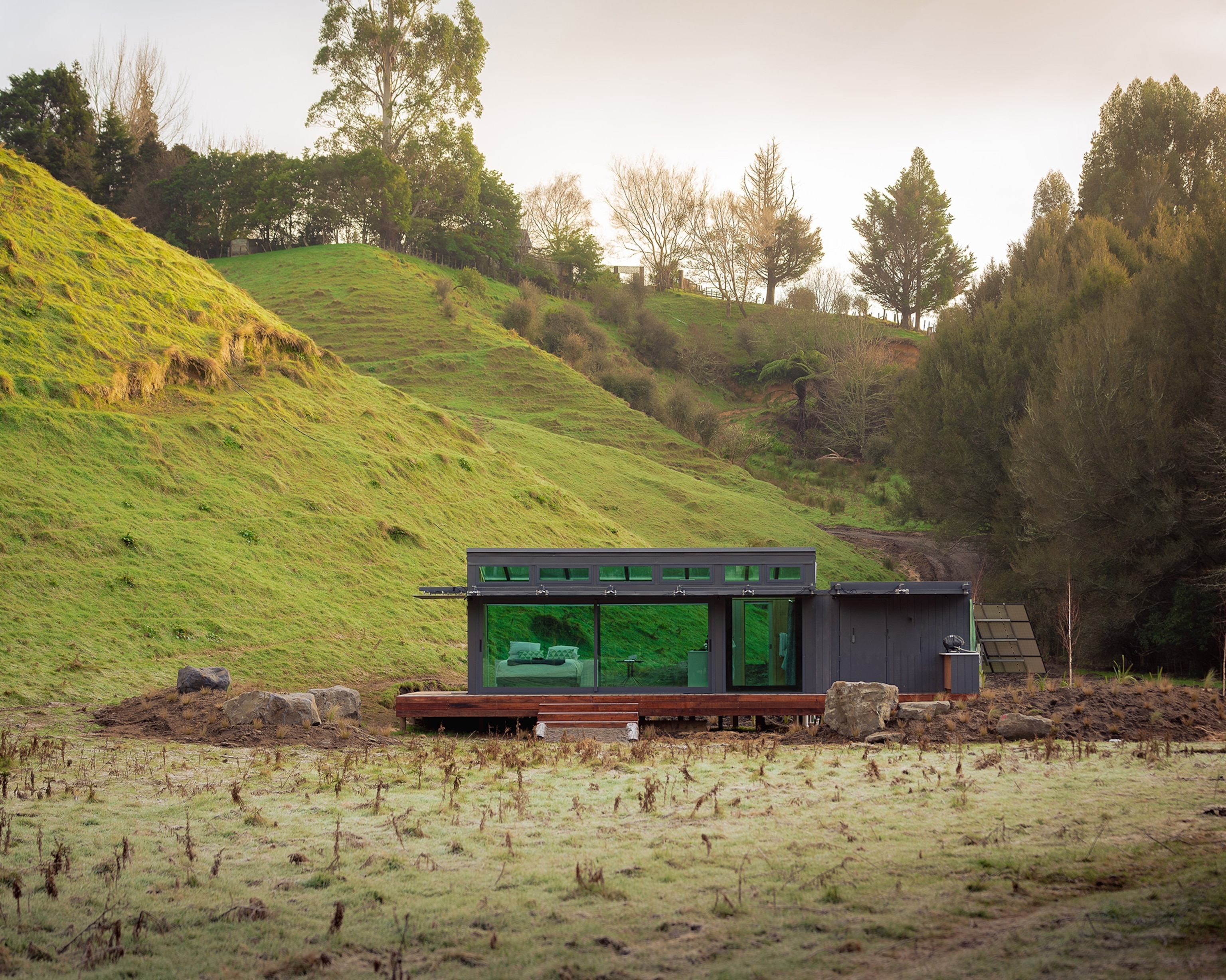 The exterior of Pāmu PurePod in Rotorua, New Zealand nestled at the bottom of a grassy hill.