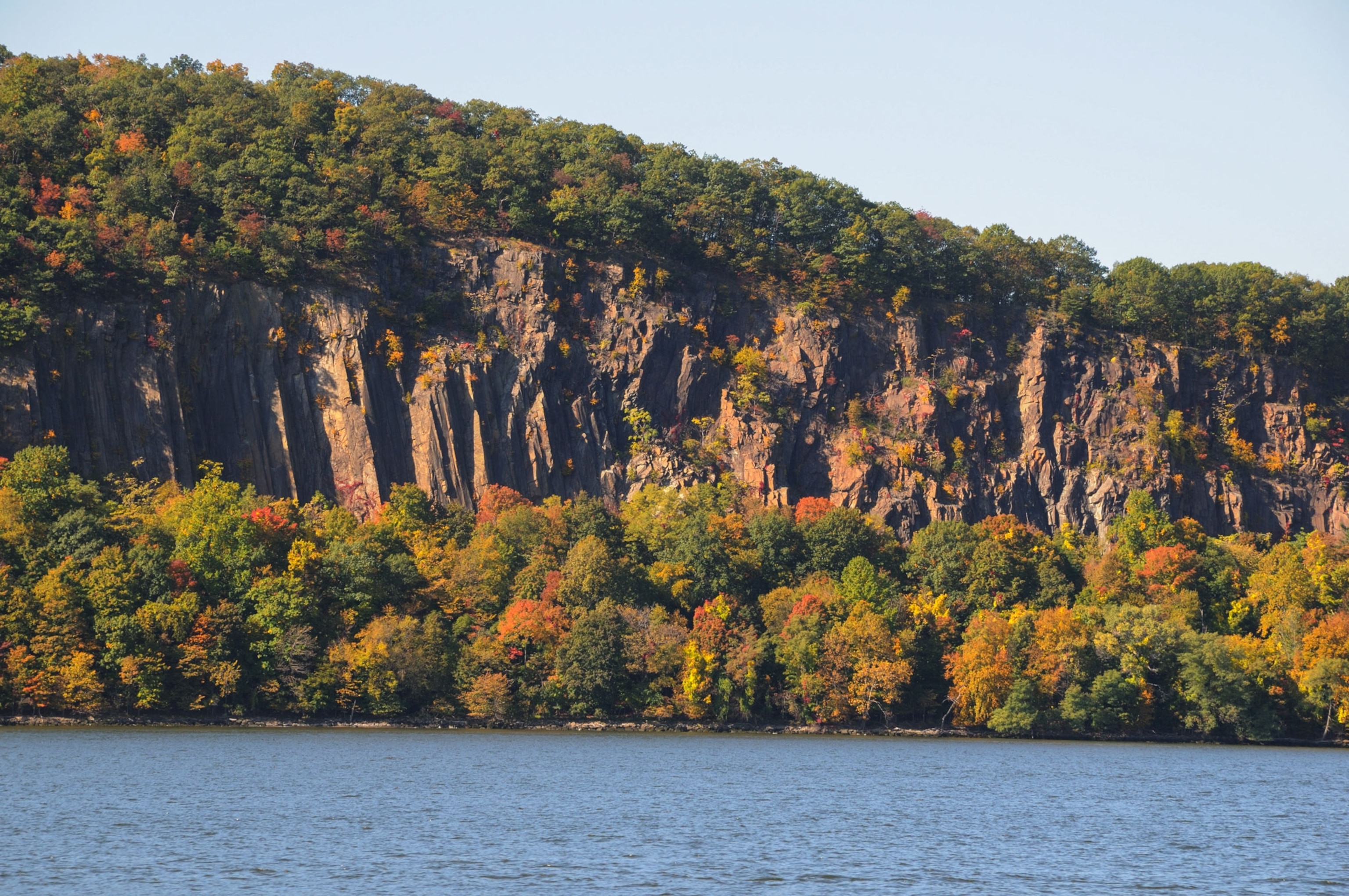 a rocky cliff with trees seen from across the Hudson River