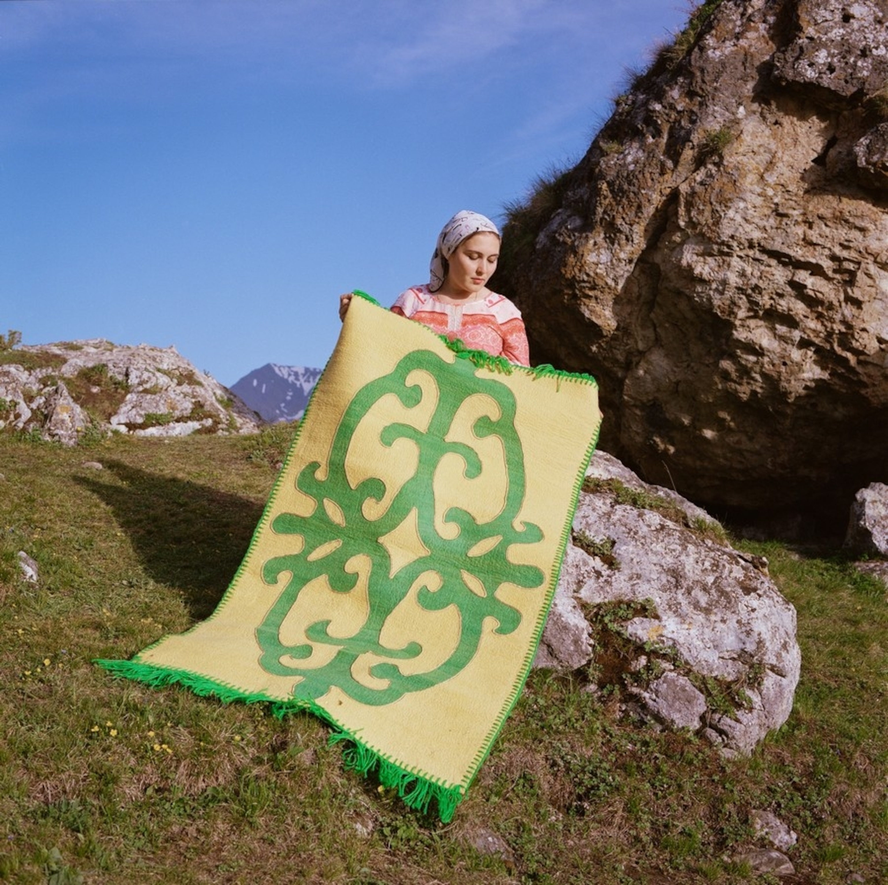a woman holds a rug with the Ingush national ornament of the 19th century in the village of Goust