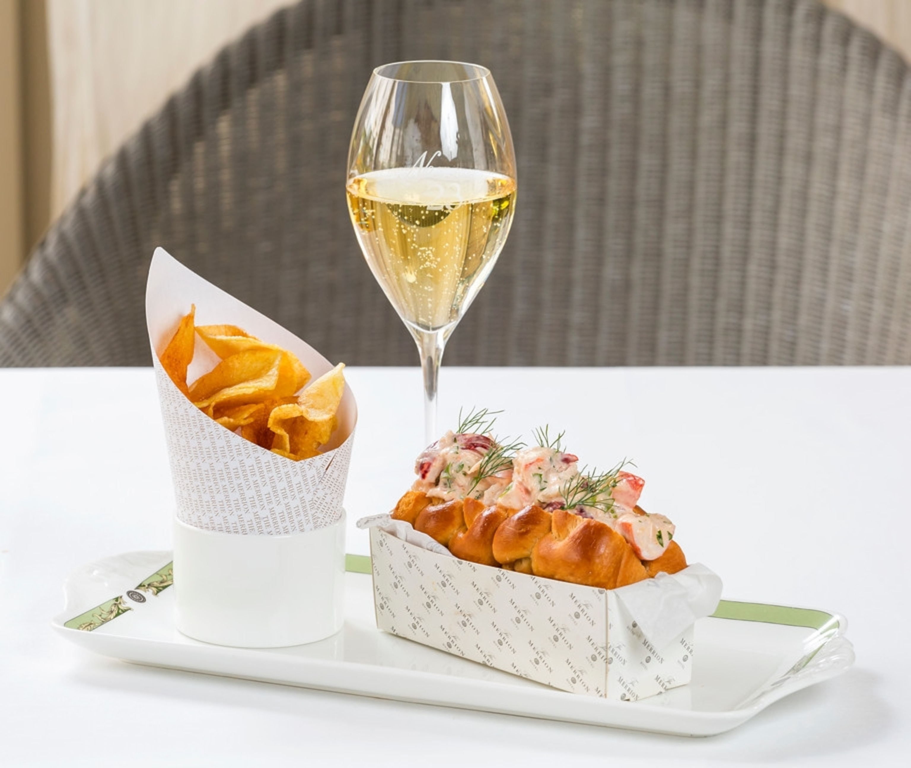 Cup of fries, a lobster roll on a plate and a glass of white wine.