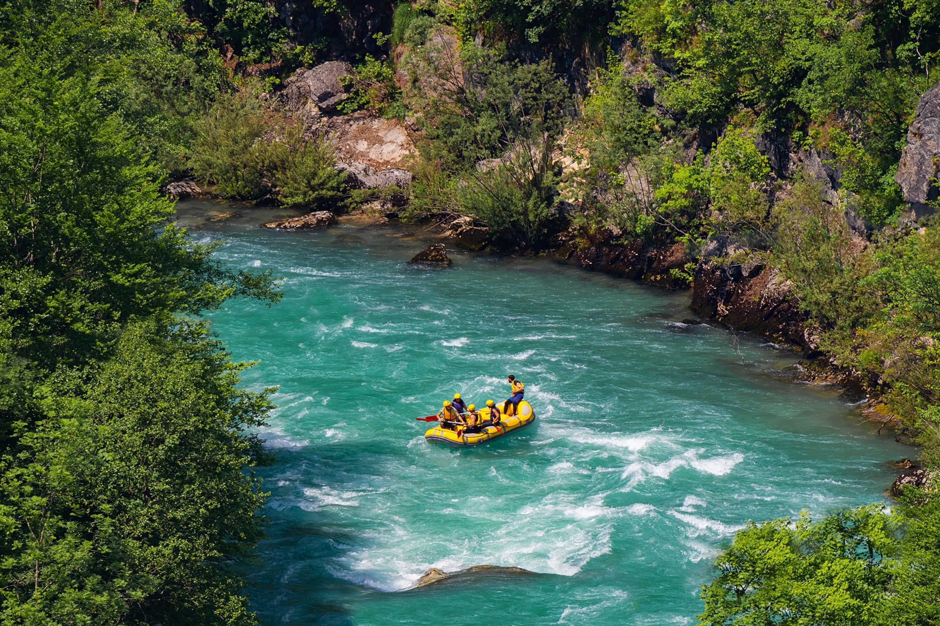 People on an inflatable yellow boat rafting down a fast flowing river