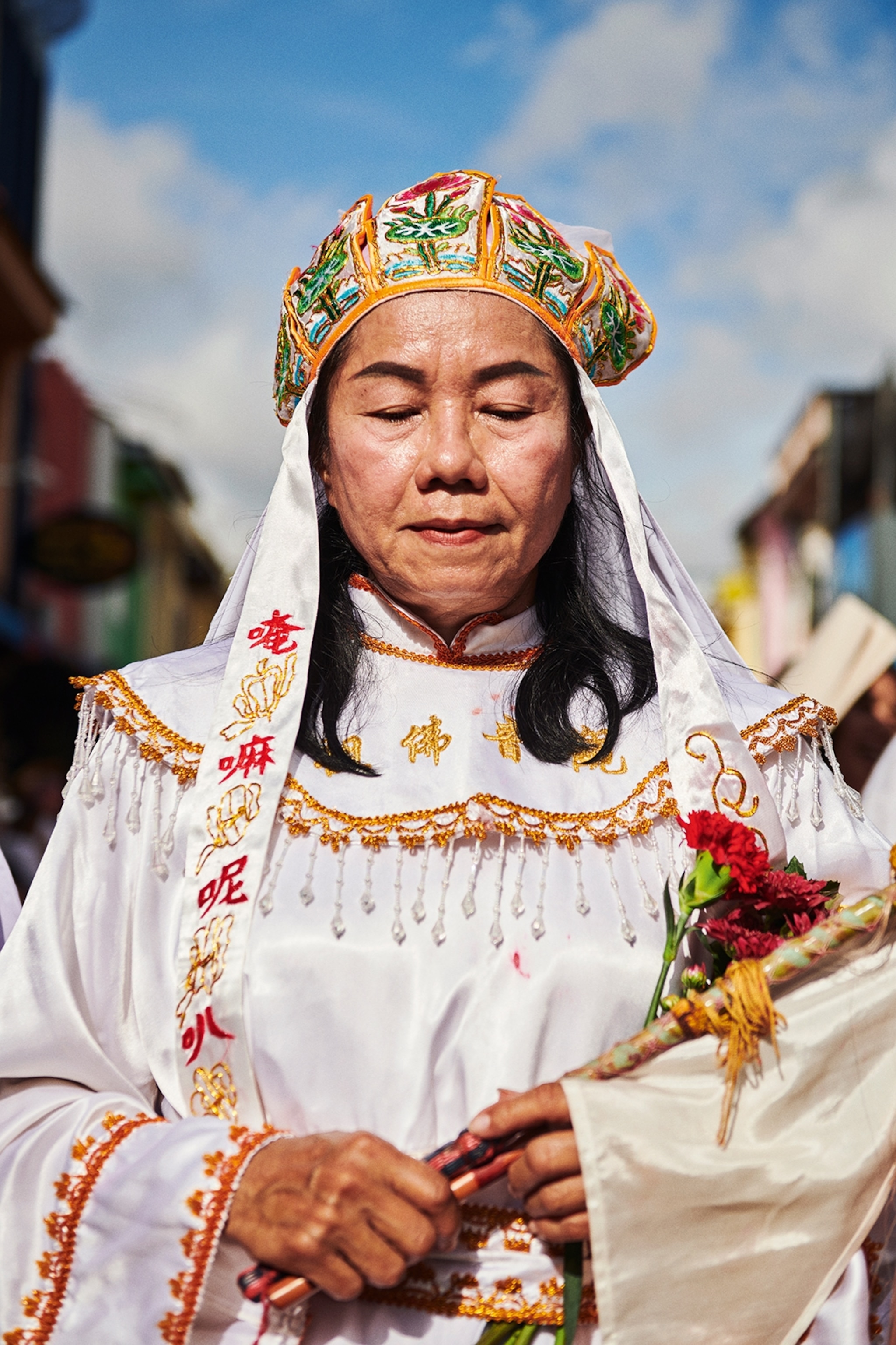 A thai woman is wearing a colourful headress and white gown with gold embroidery.