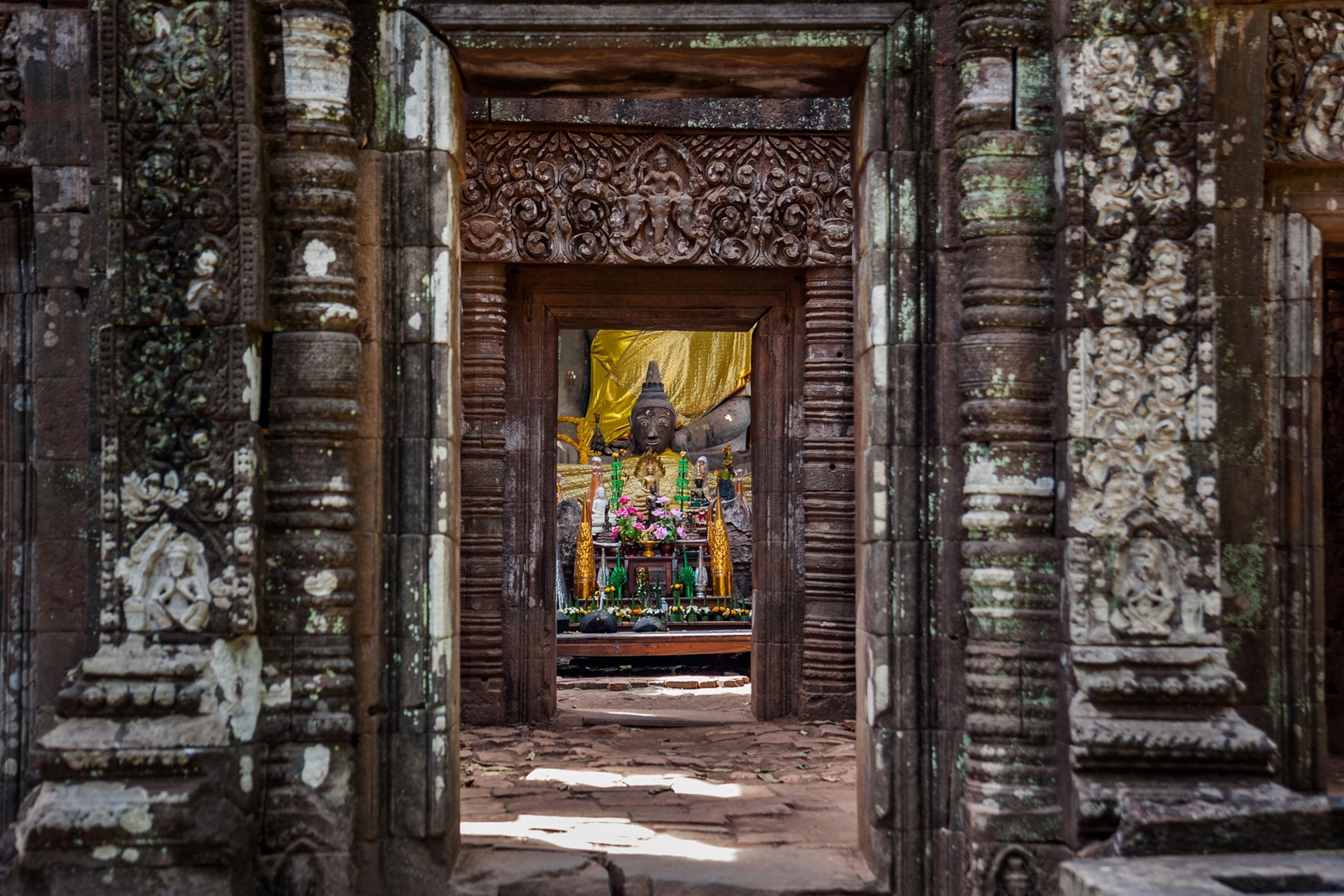 Inside a stone temple with elaborate stone carvings and buddhist statues in the middle.