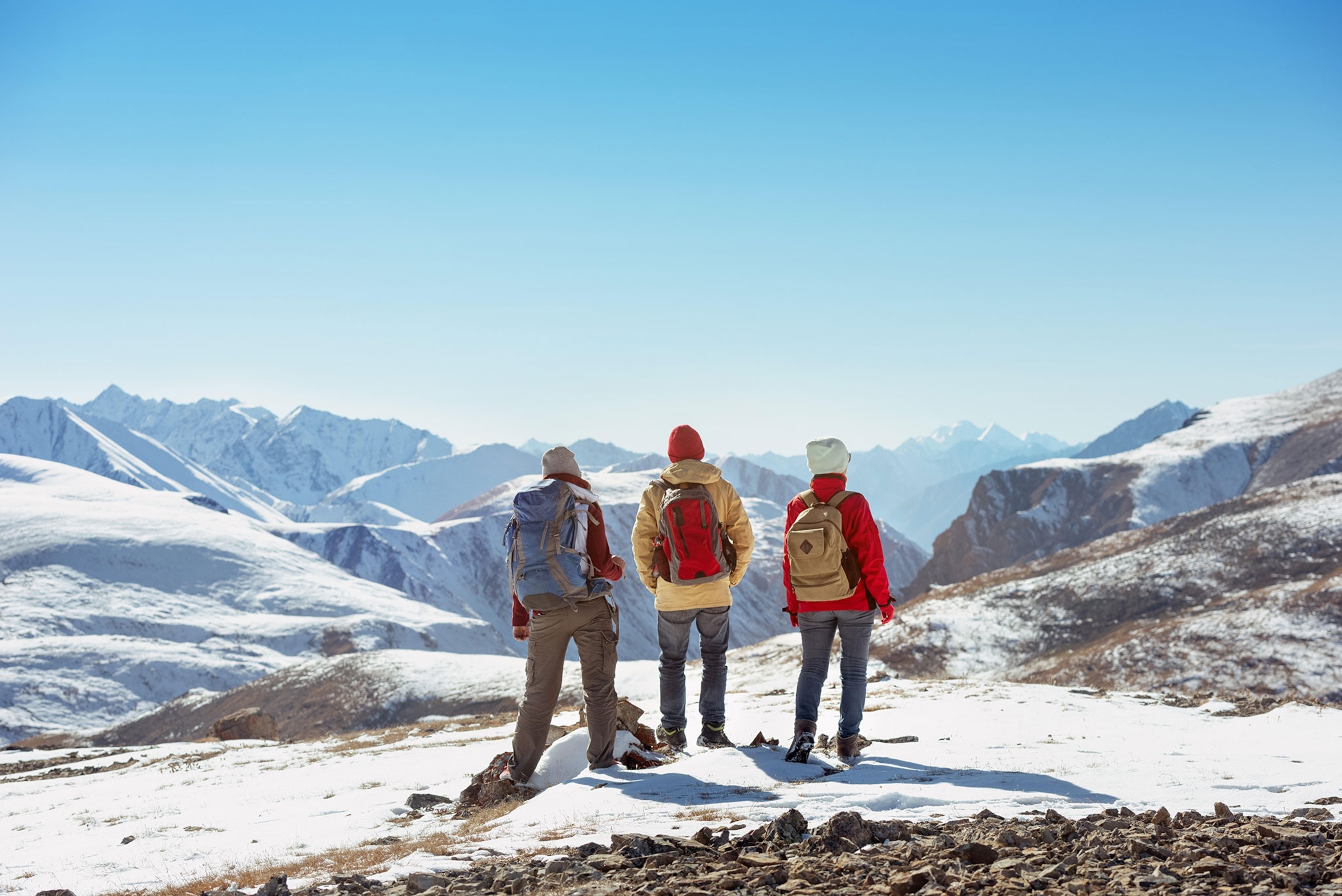 Three people stand on snow looking out across the top of a mountain.