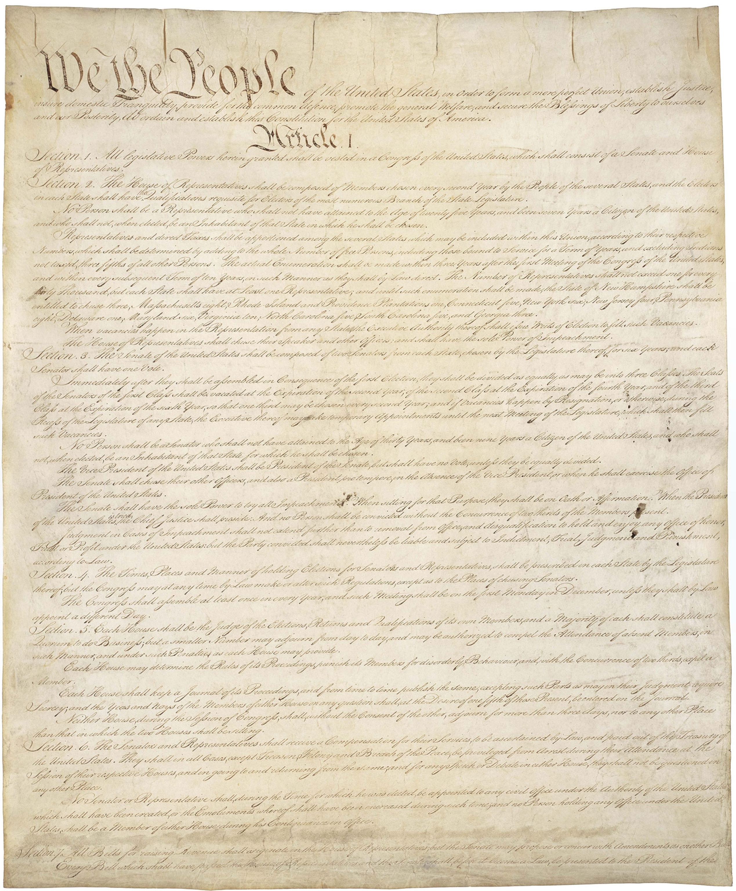 An old, tannish piece of paper with calligraphy starting with "We the People"