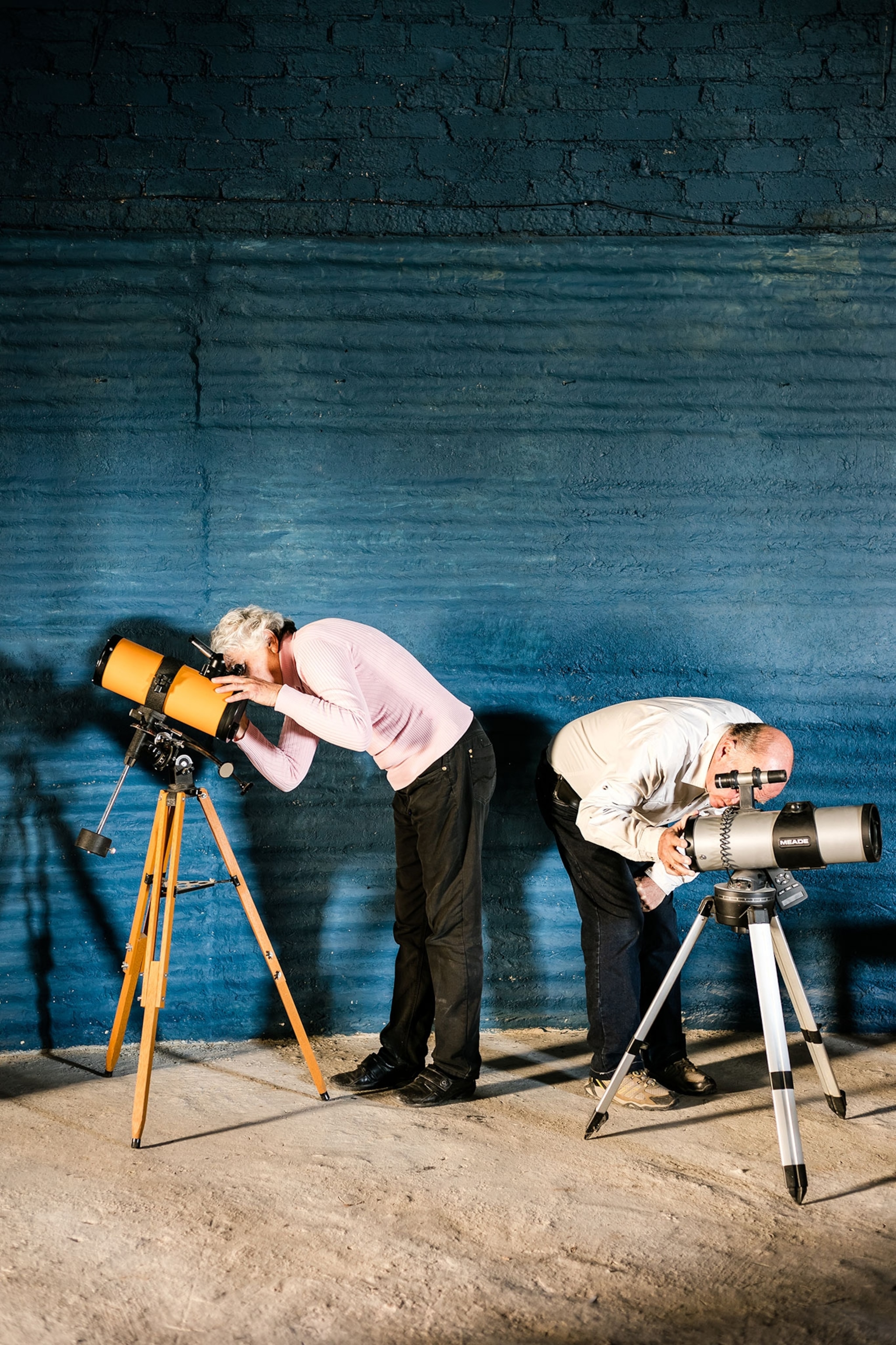 two people looking through telescopes.