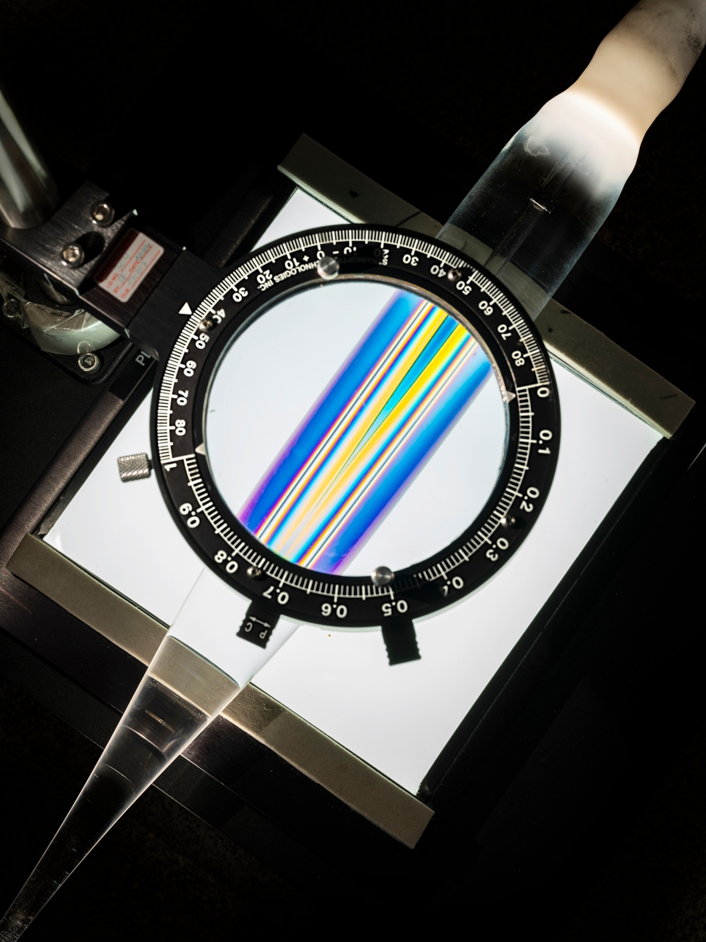 a rainbow coloring of glass seen through a lens with a black circle edge with white etched numbers.