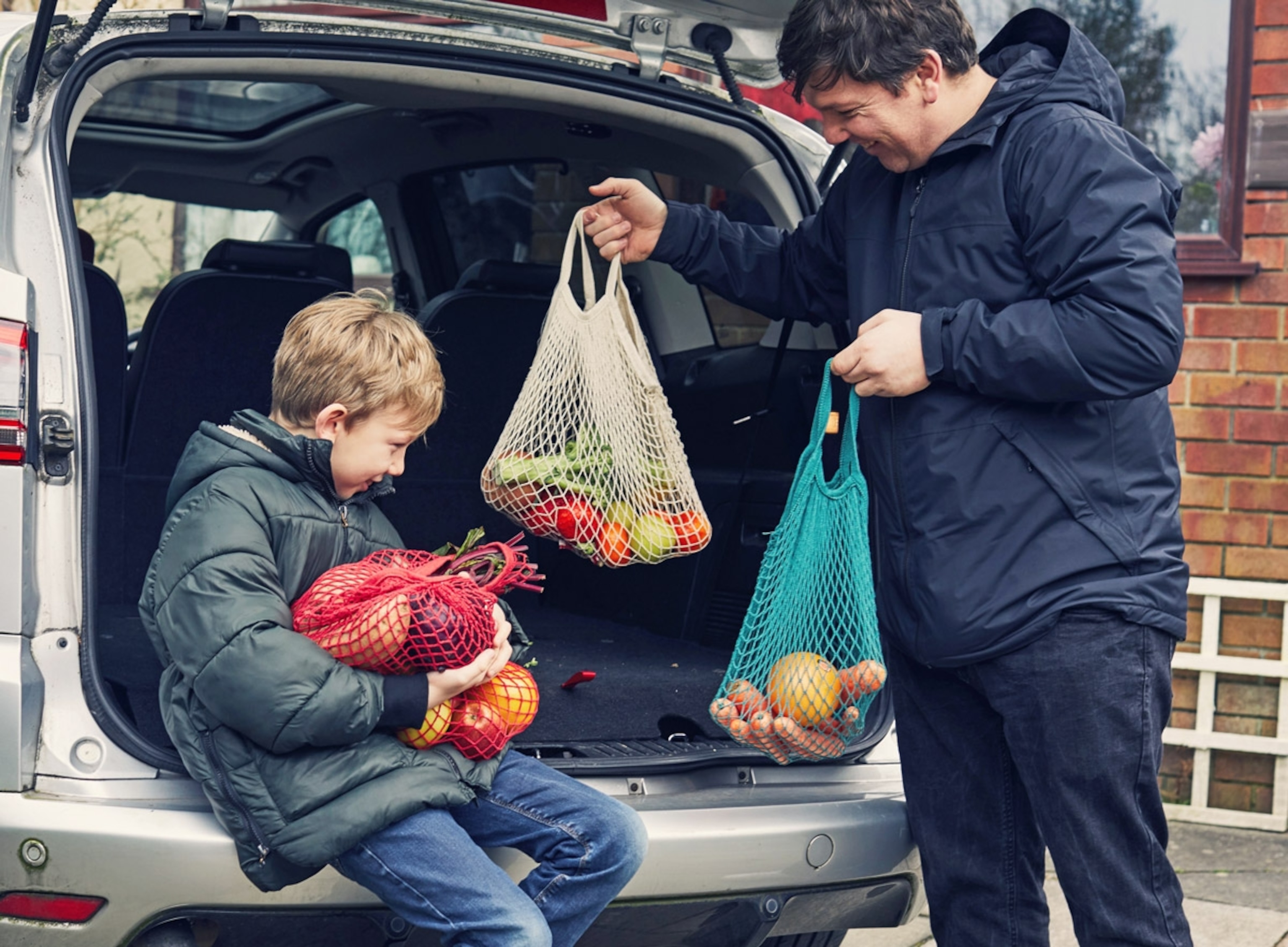 Happy smiling Father and son carrying shopping in reusable string bags. United Kingdom