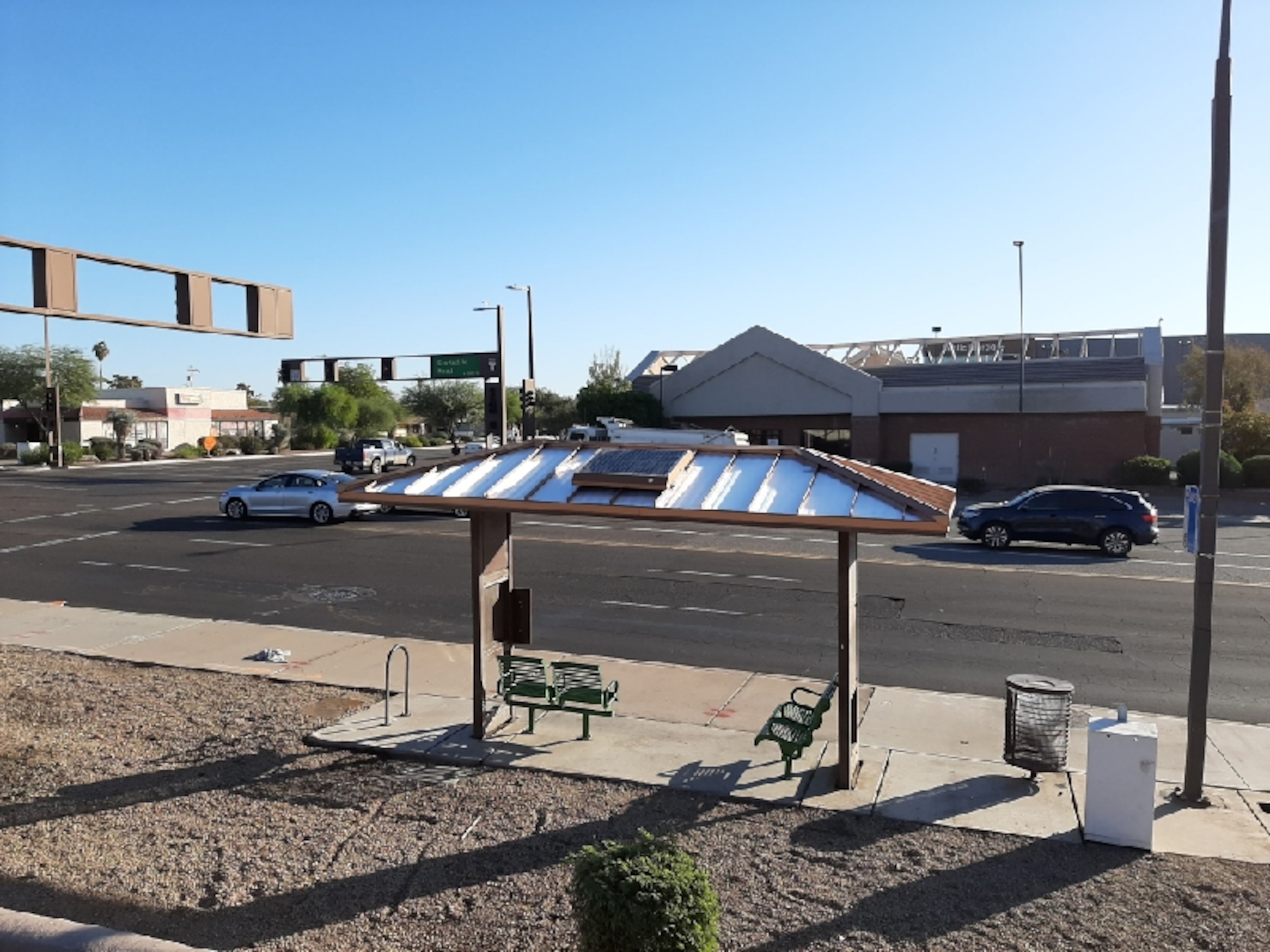 a thin white sticker-like film on top of a bus shelter in a bright and crowded intersection in Arizona.