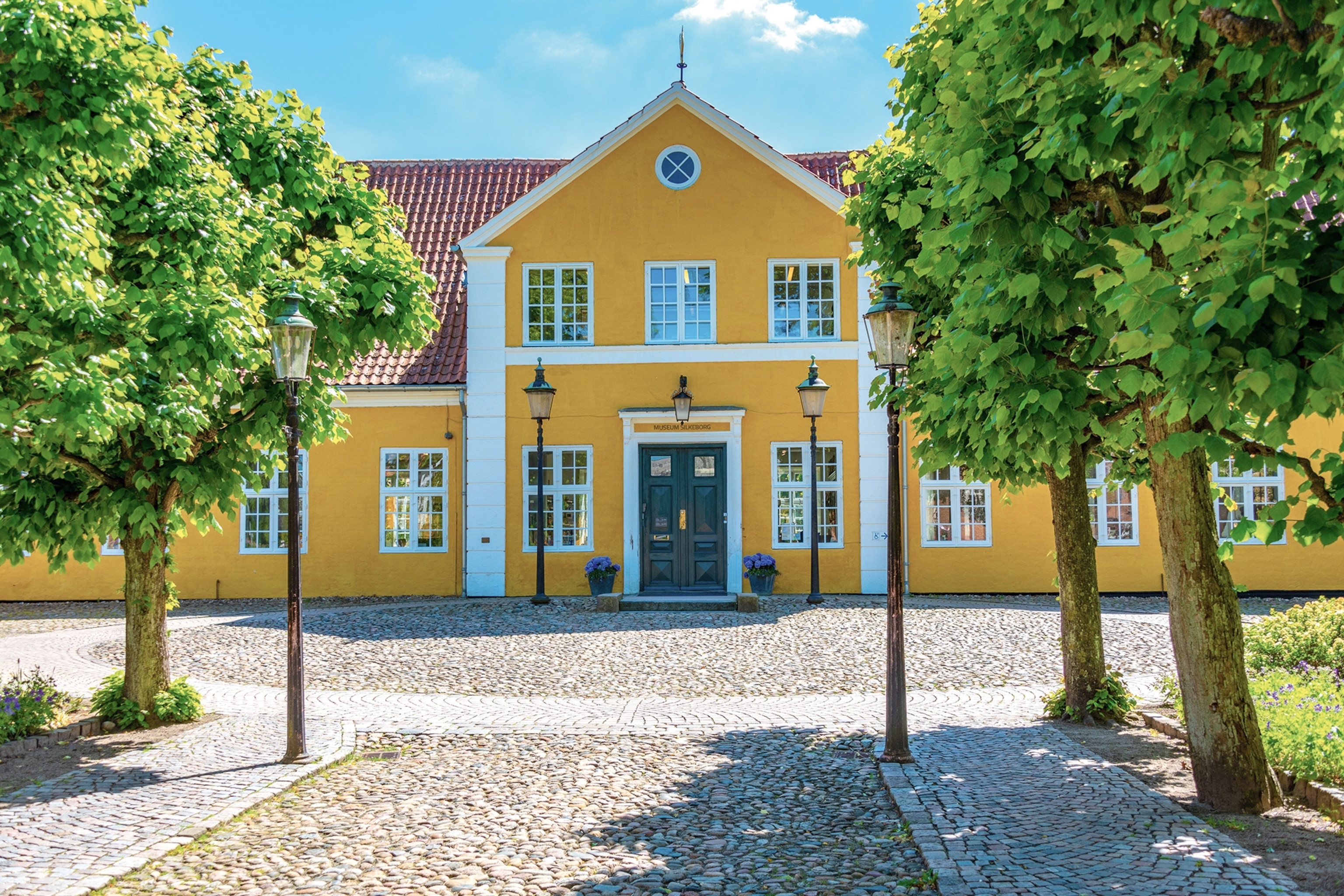 Yellow and white brick building with trees in front with blue skies