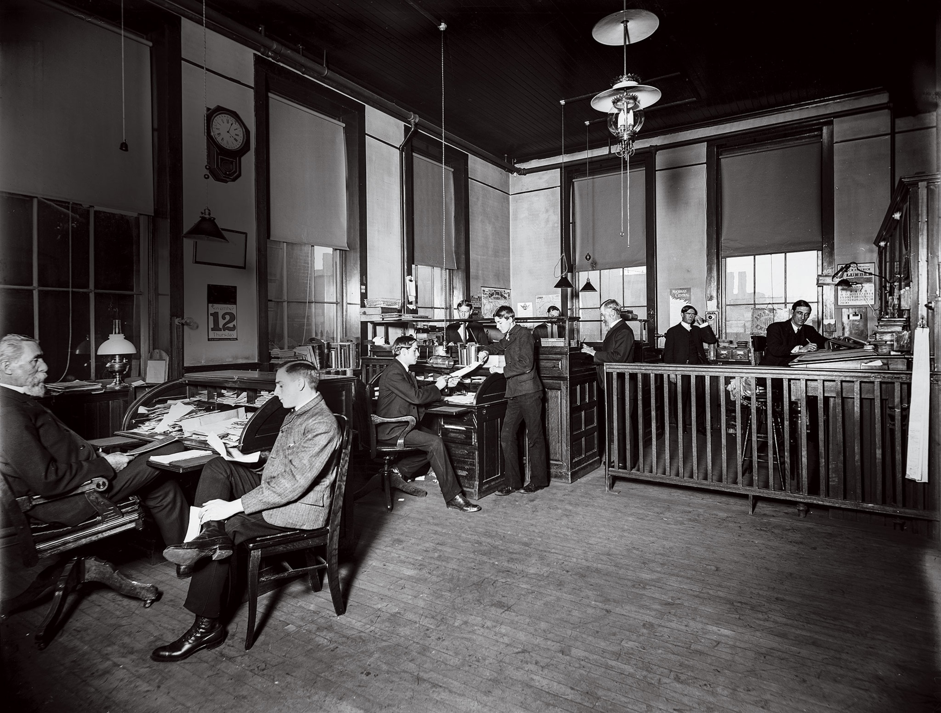 A black-and-white image of men working in an office, some sitting some standing