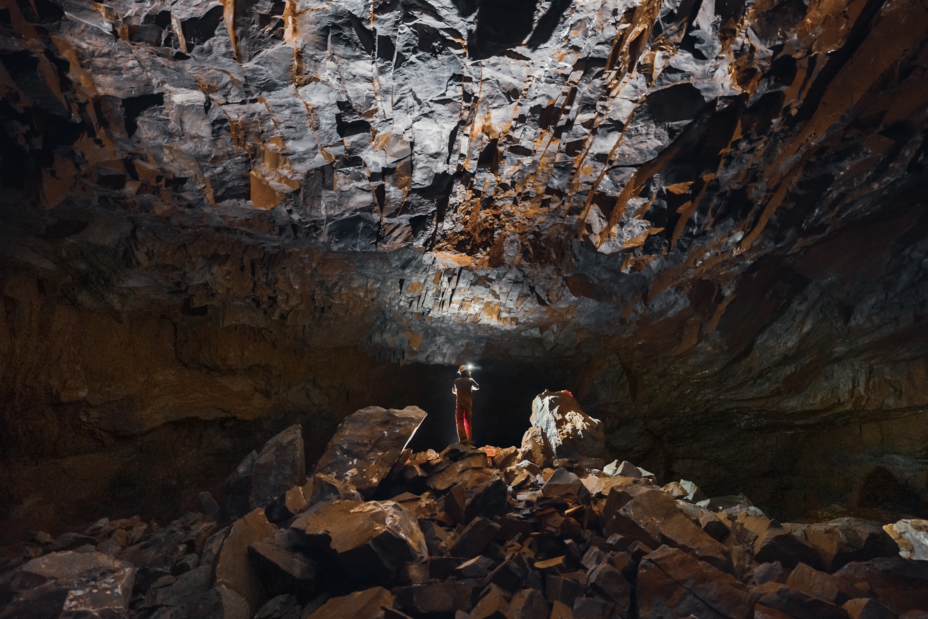 Picture of person in head hat standing under lower cave ceiling.
