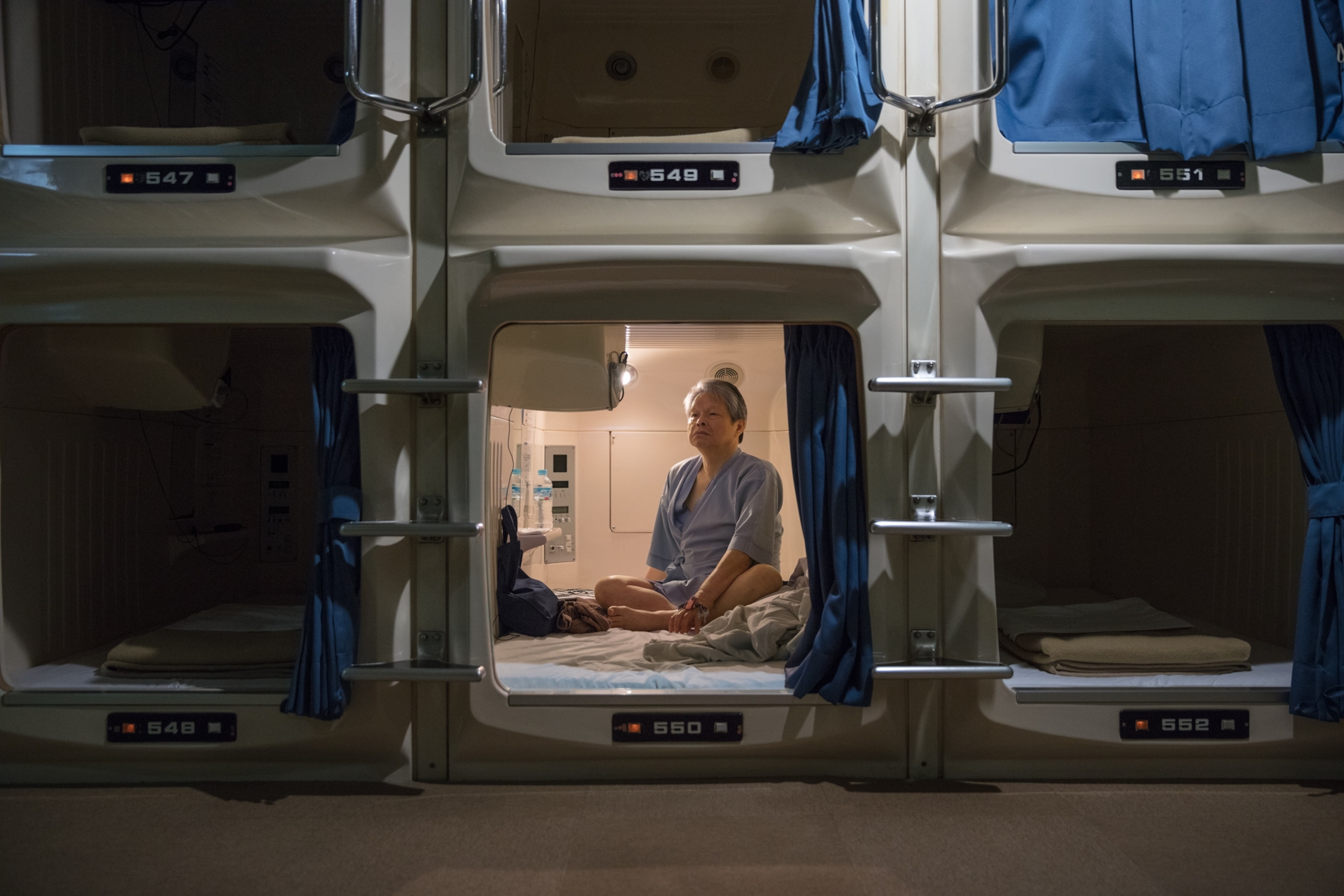 man sitting inside his capsule hotel bedroom