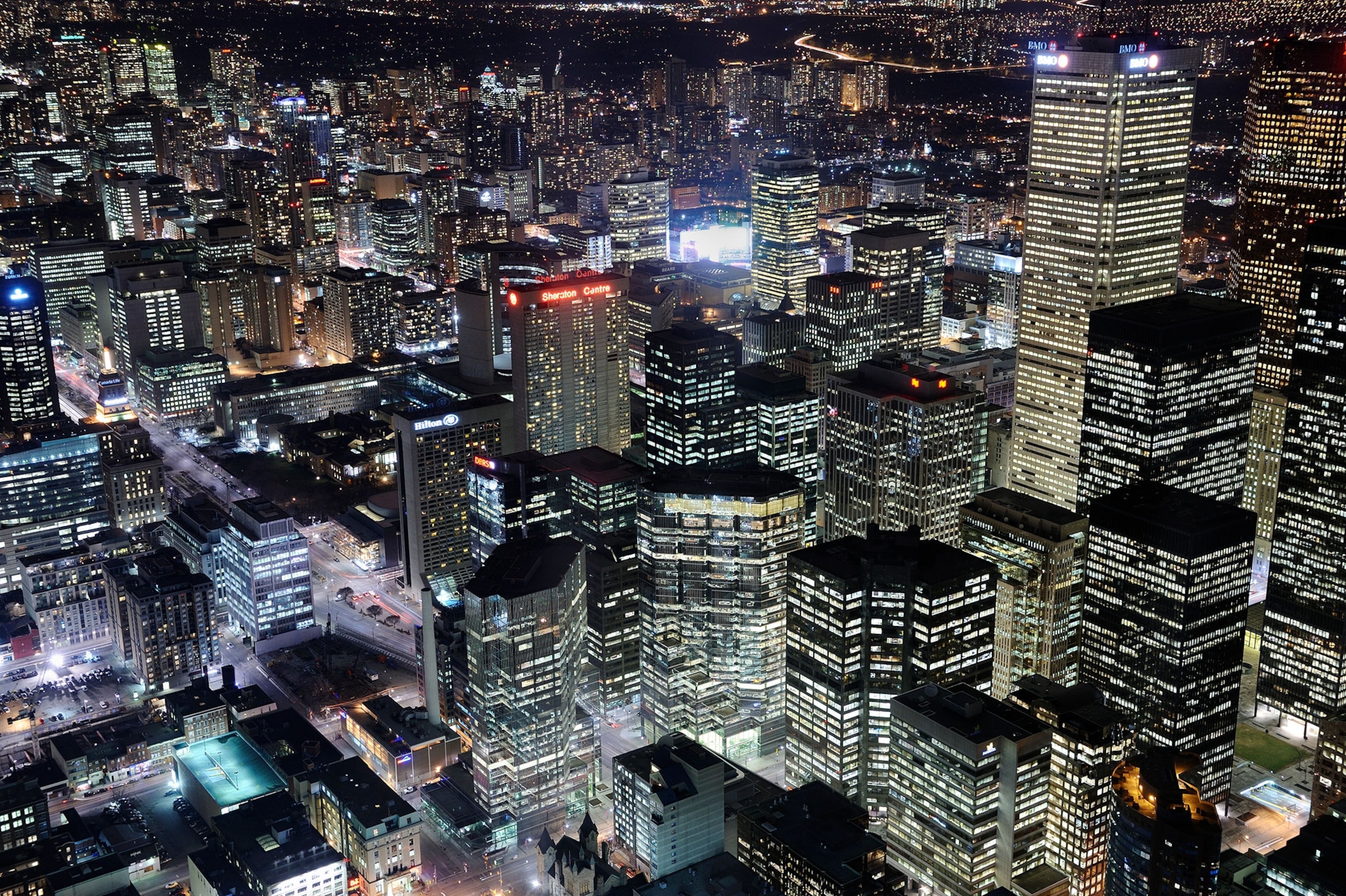 Dozens of sky scrappers at night with hundreds of white, light blue and purple illuminated windows and other glowing signs.