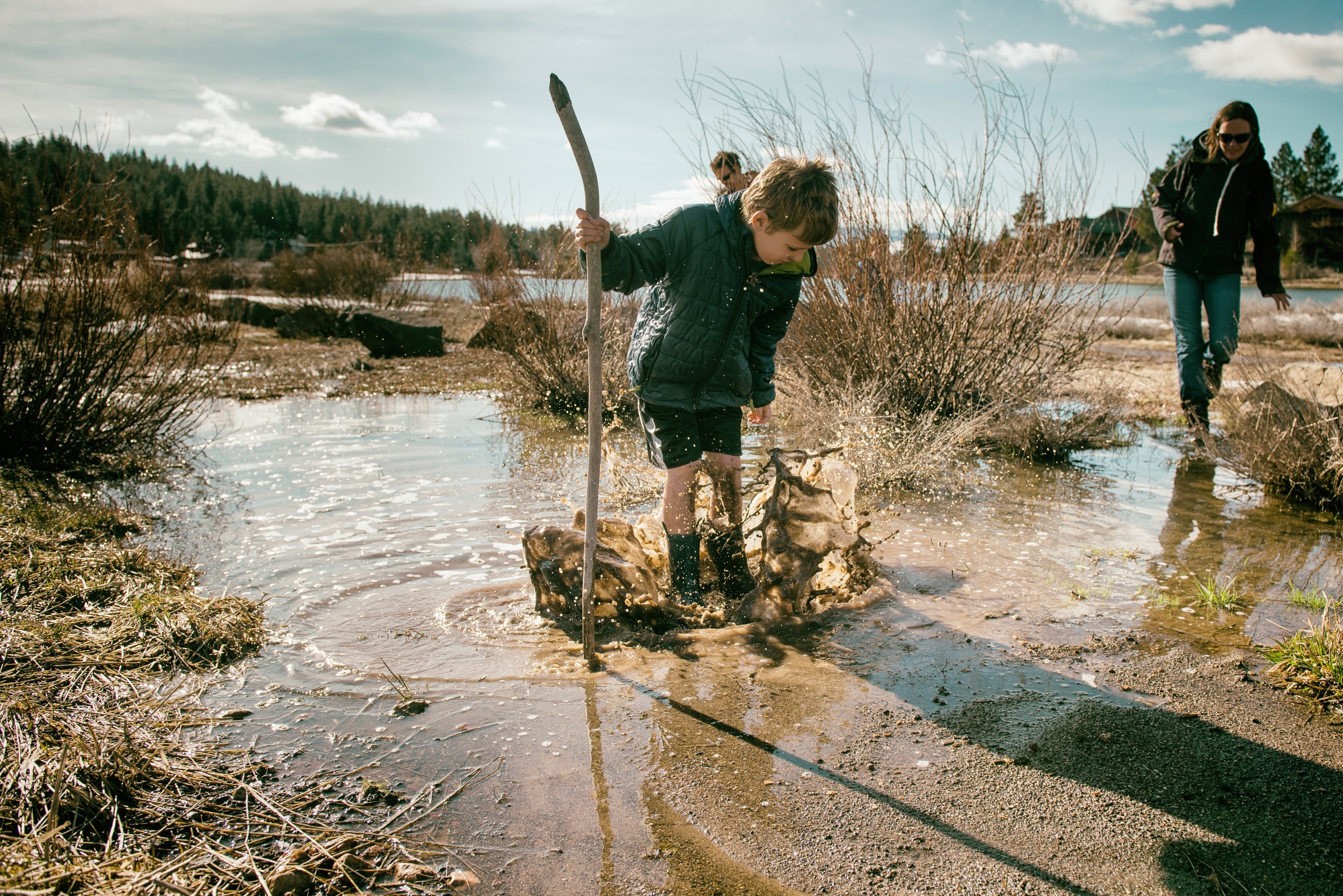 Child making a big splash as mom comes to get him in the mud in a meadow during Spring