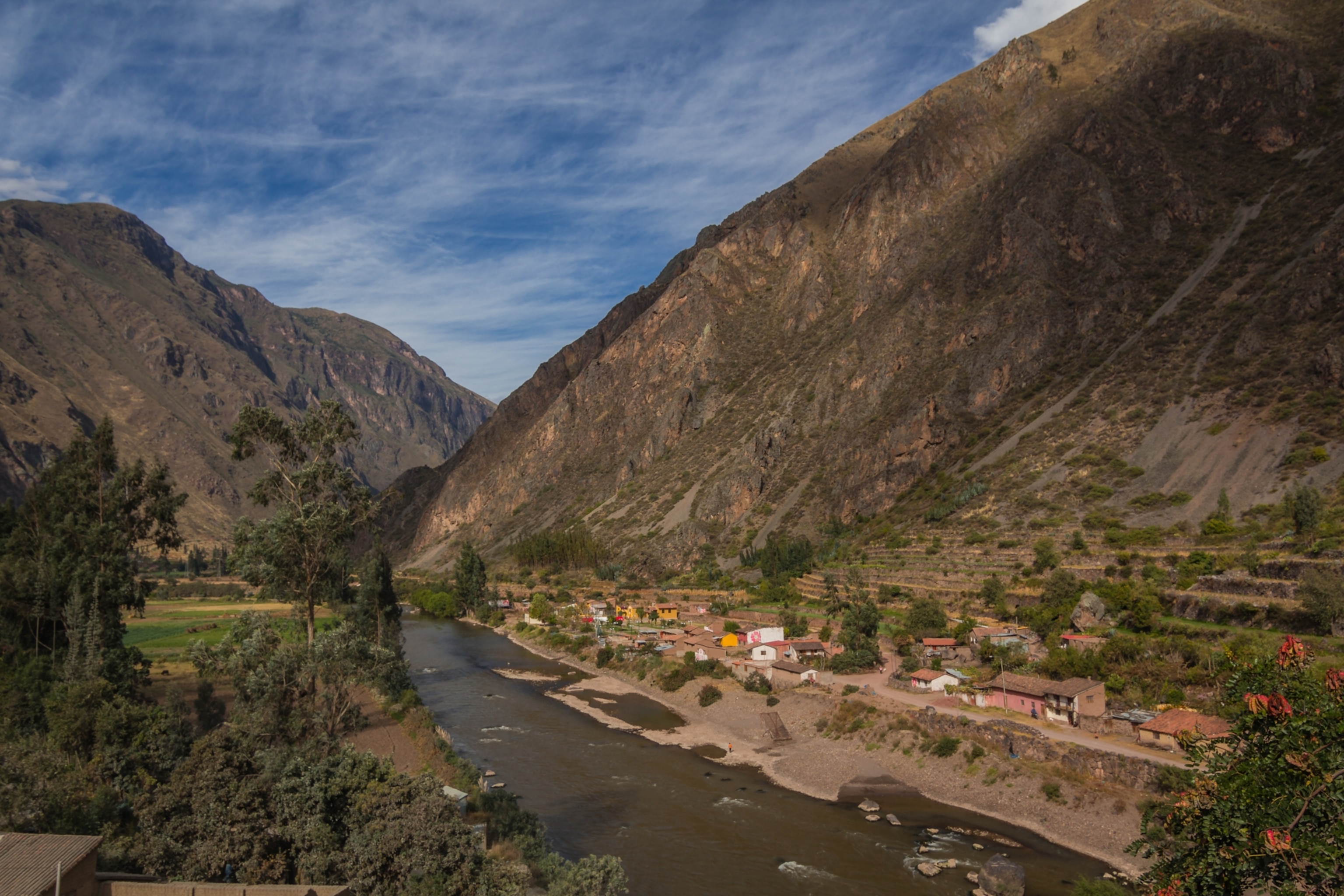 Panoramic view of Urubamba River, with a village between the water's edge and mountain valley