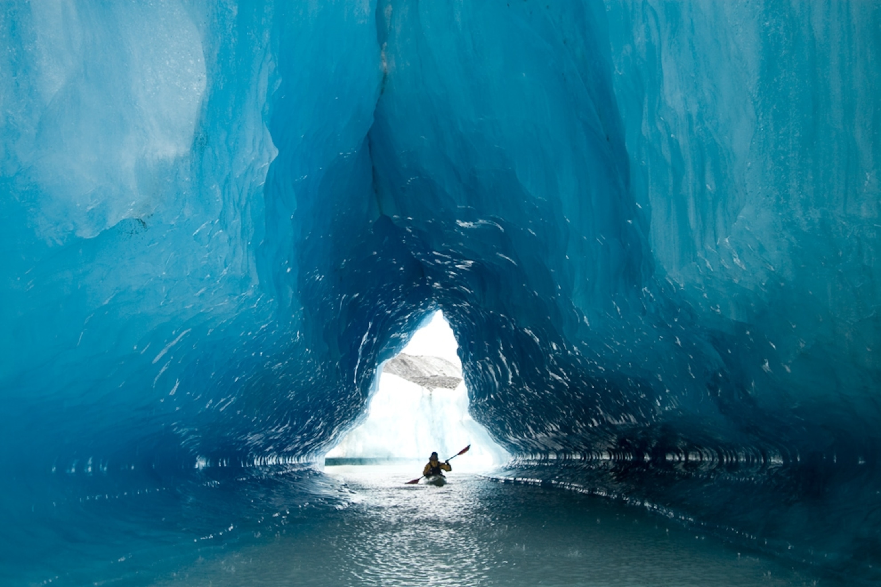 Sea kayaker paddles through an ice cave