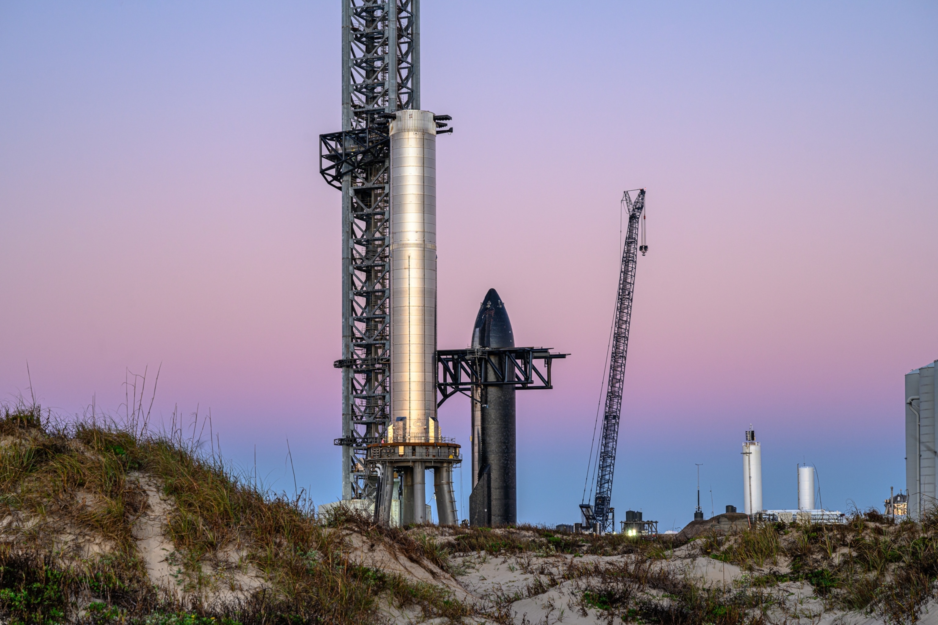 Picture of Starship 20 beside Super Heavy Booster 4 against a blue and purple sky.
