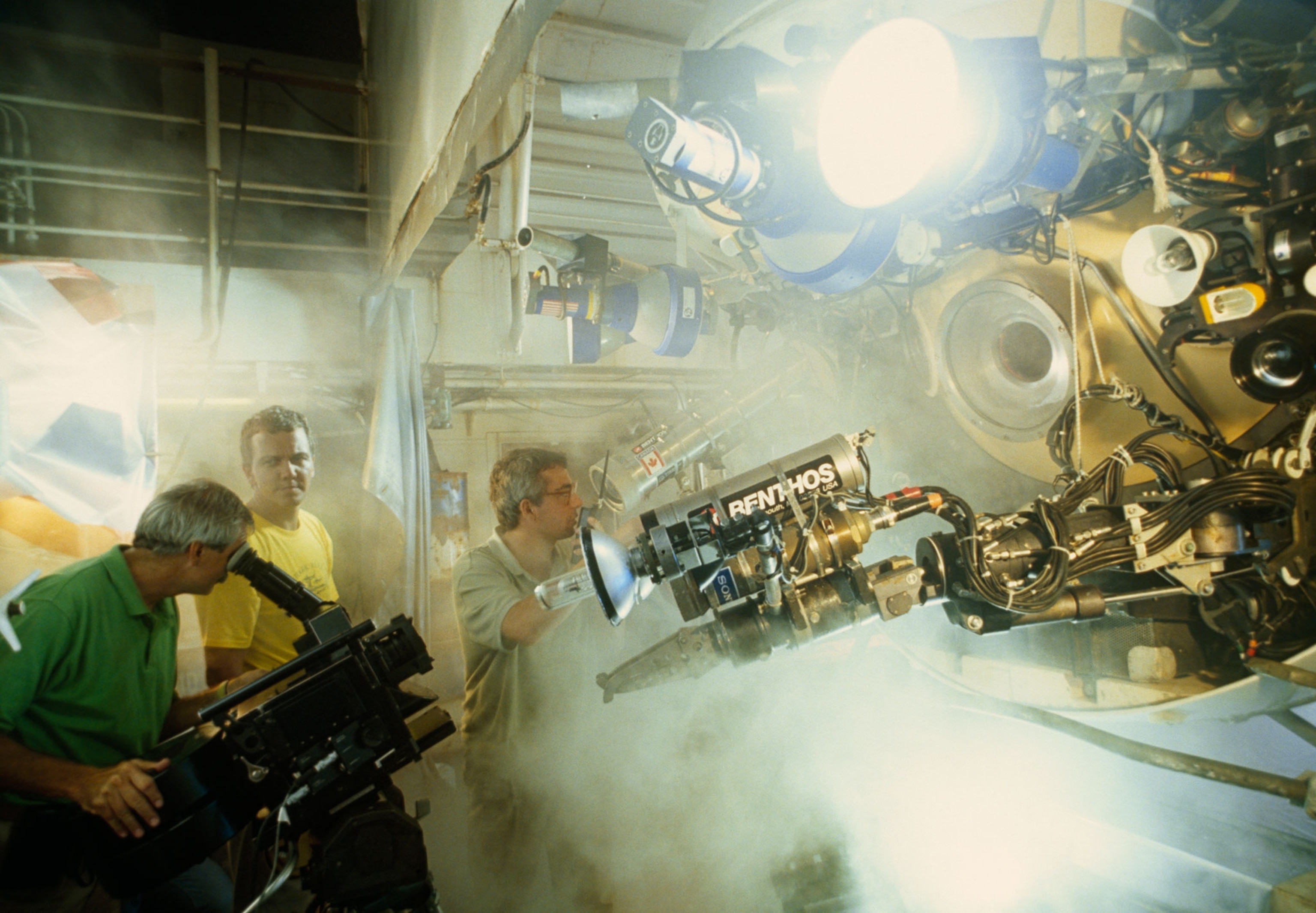 Group of three men surrounded by cameras and fog record out of research vessel.