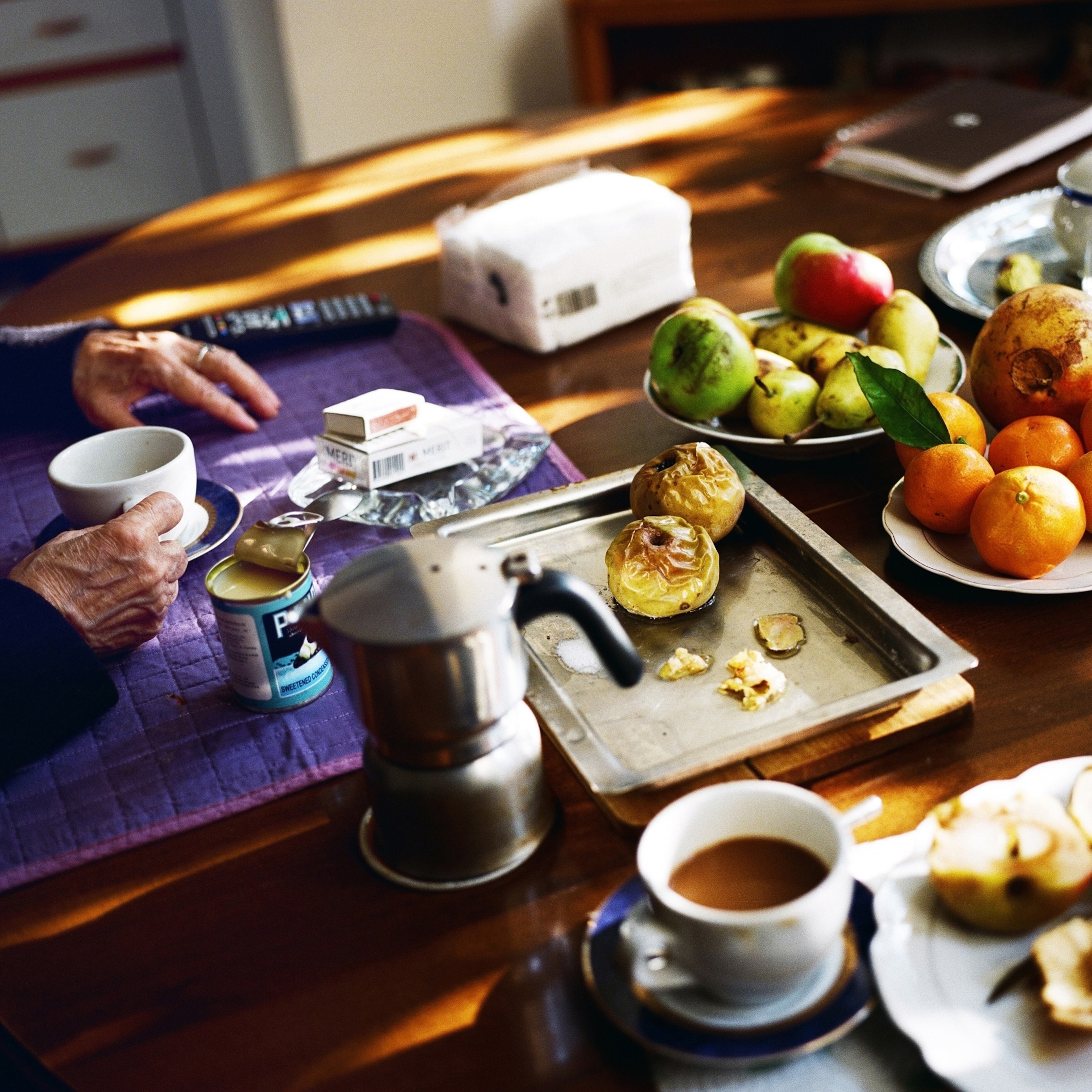 A women holds a coffee cup at a table filled with fruits and pastry.