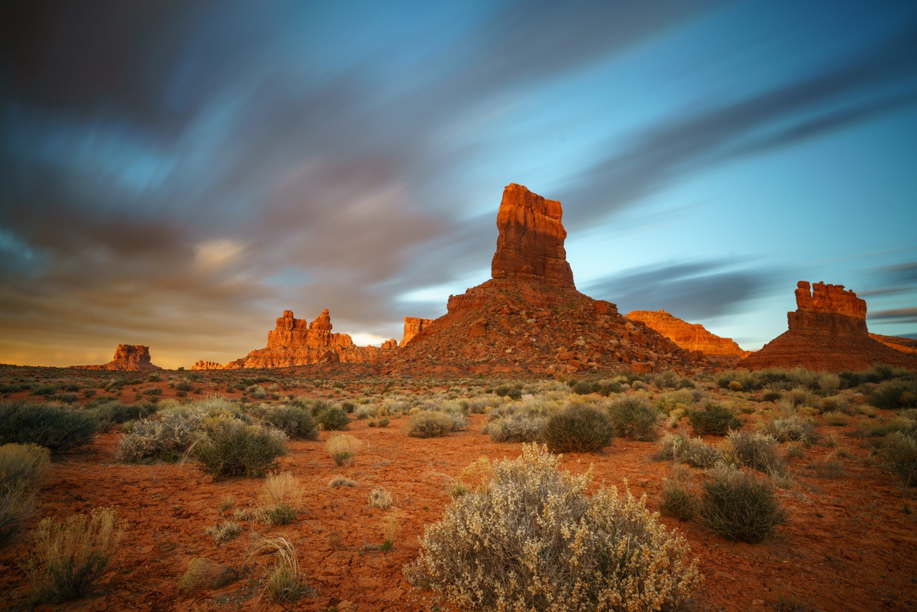 Dramatic morning light strikes rocky butte formations, which glow red against pale blue sky.
