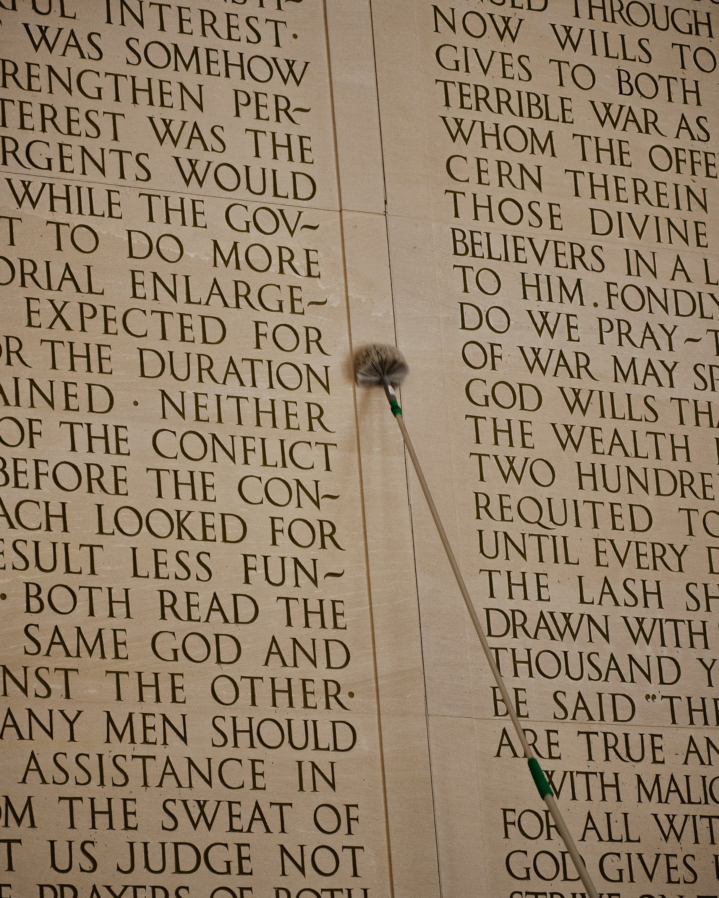 A mop held by an NPS worker cleans the carved inscription of Lincoln's second inaugural address at the Lincoln Memorial