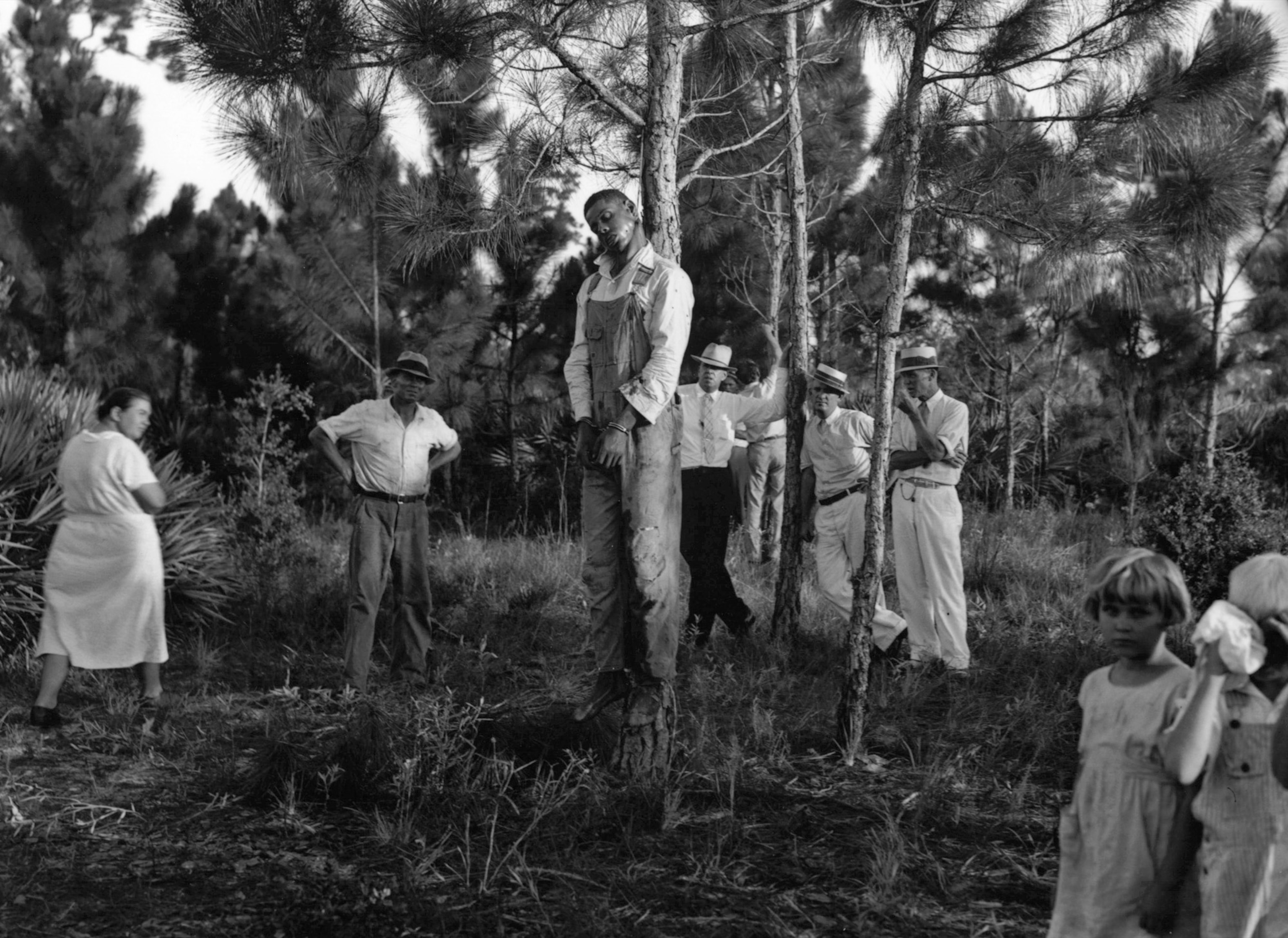 an African American man hanging from a tree with white spectators around